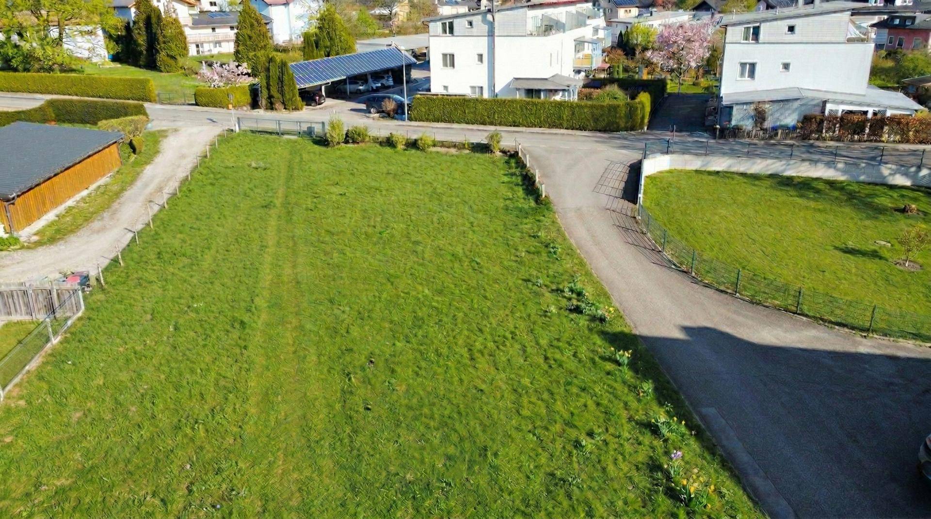 Luftaufnahme eines grünen Grundstücks mit angrenzender Straße und modernen Wohnhäusern in der Umgebung.