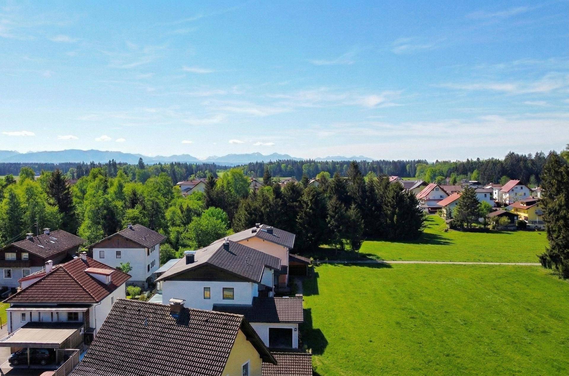 Weitläufige Wohnsiedlung mit grünen Flächen und Wäldern, im Hintergrund sind Berge sichtbar.