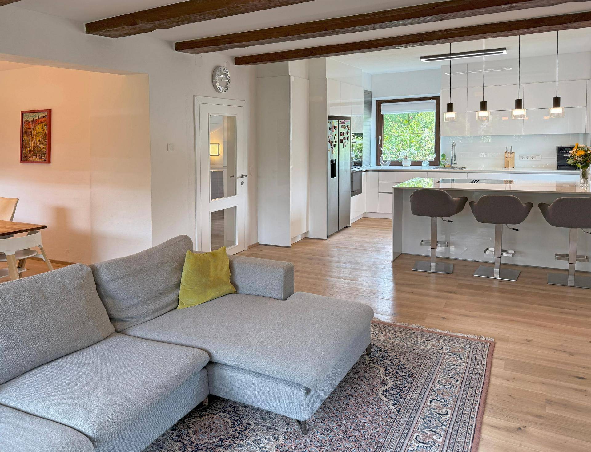 Offener Wohnbereich mit bequemer Couch, Holzbalken und direktem Zugang zur modernen Küche.