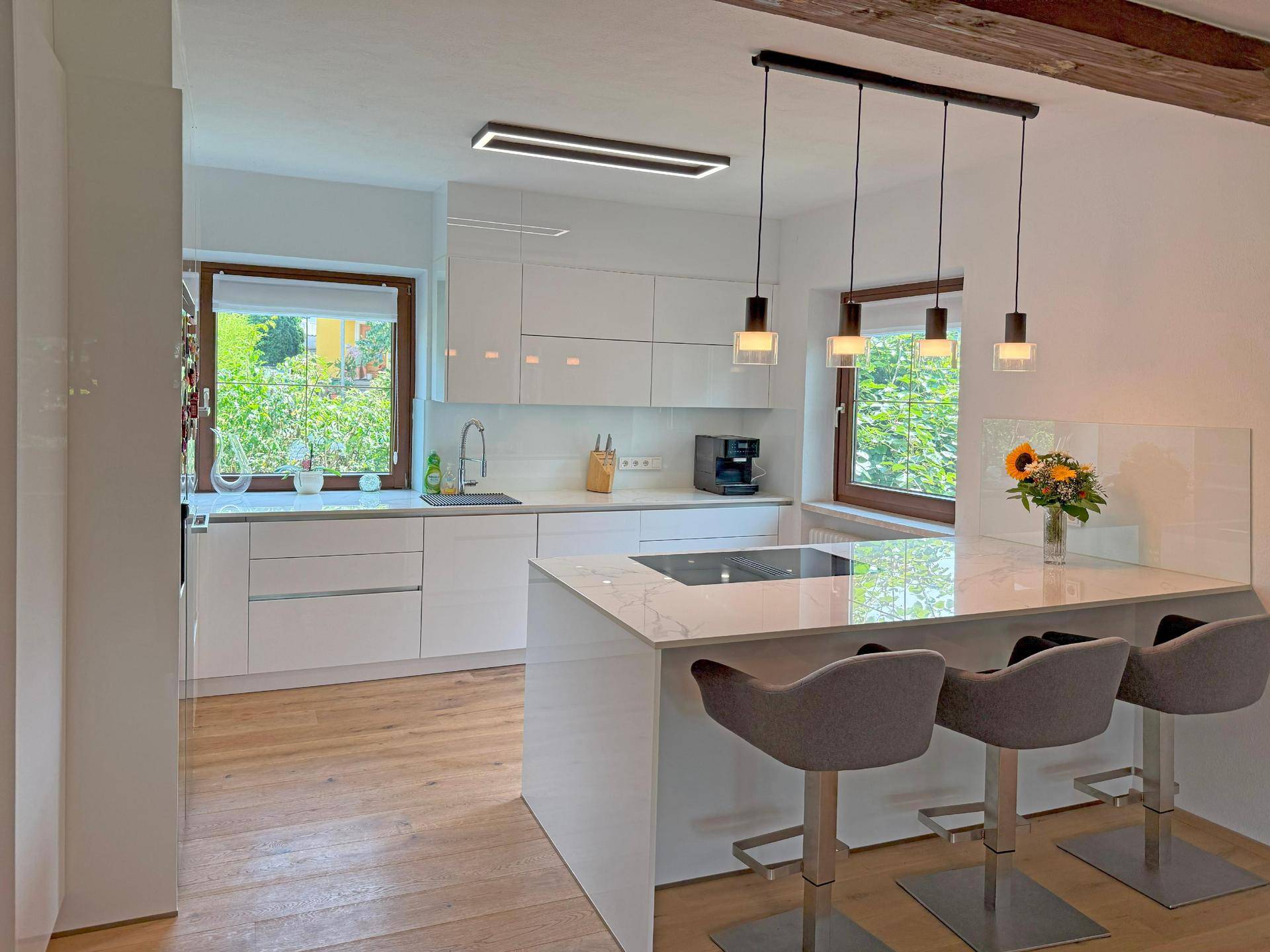 Moderne weiße Küche mit Kochinsel, Barhockern und Blick ins Grüne.