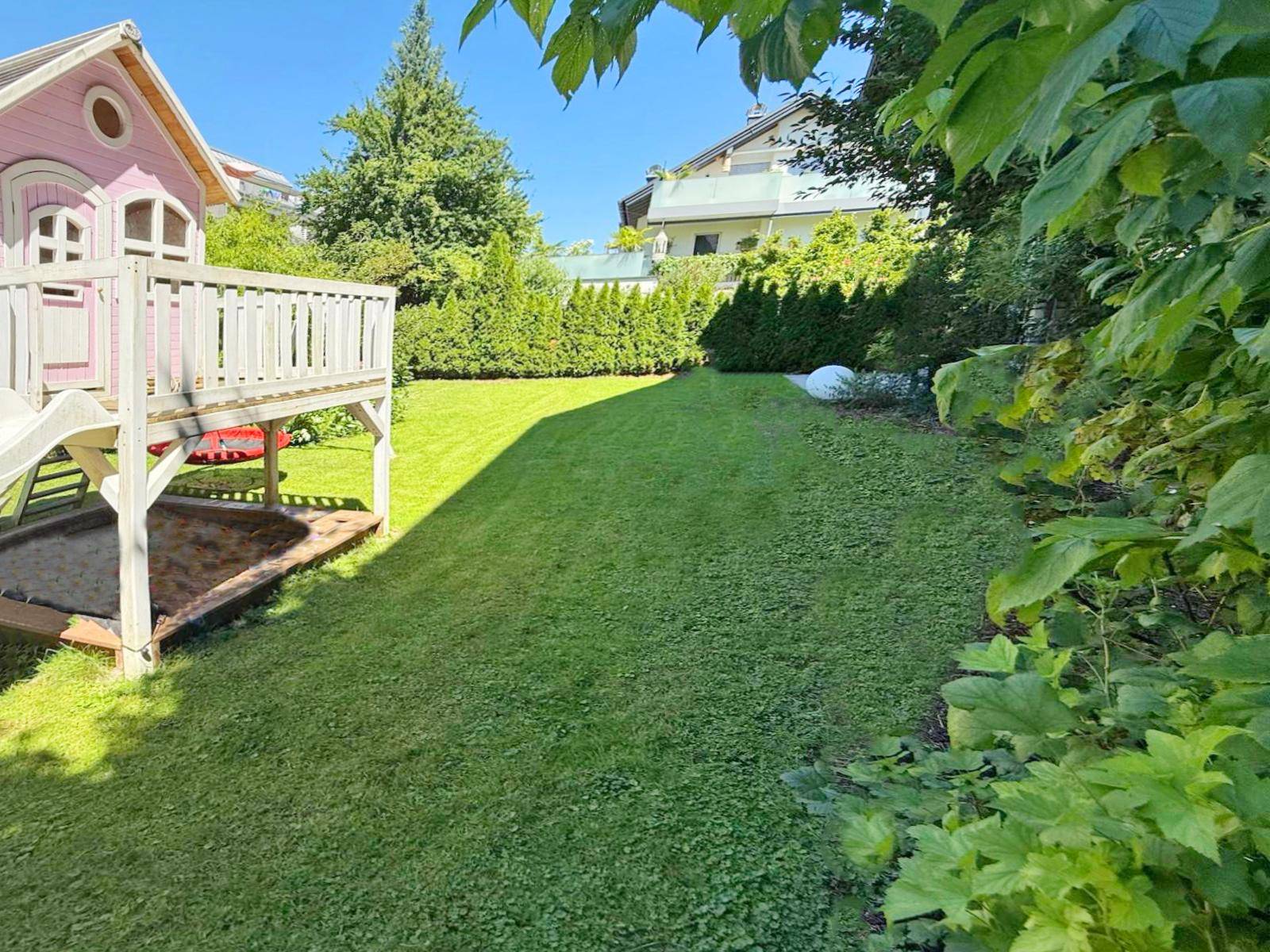 Sonniger Garten mit Spielbereich und Sandkasten, umgeben von grünen Hecken.