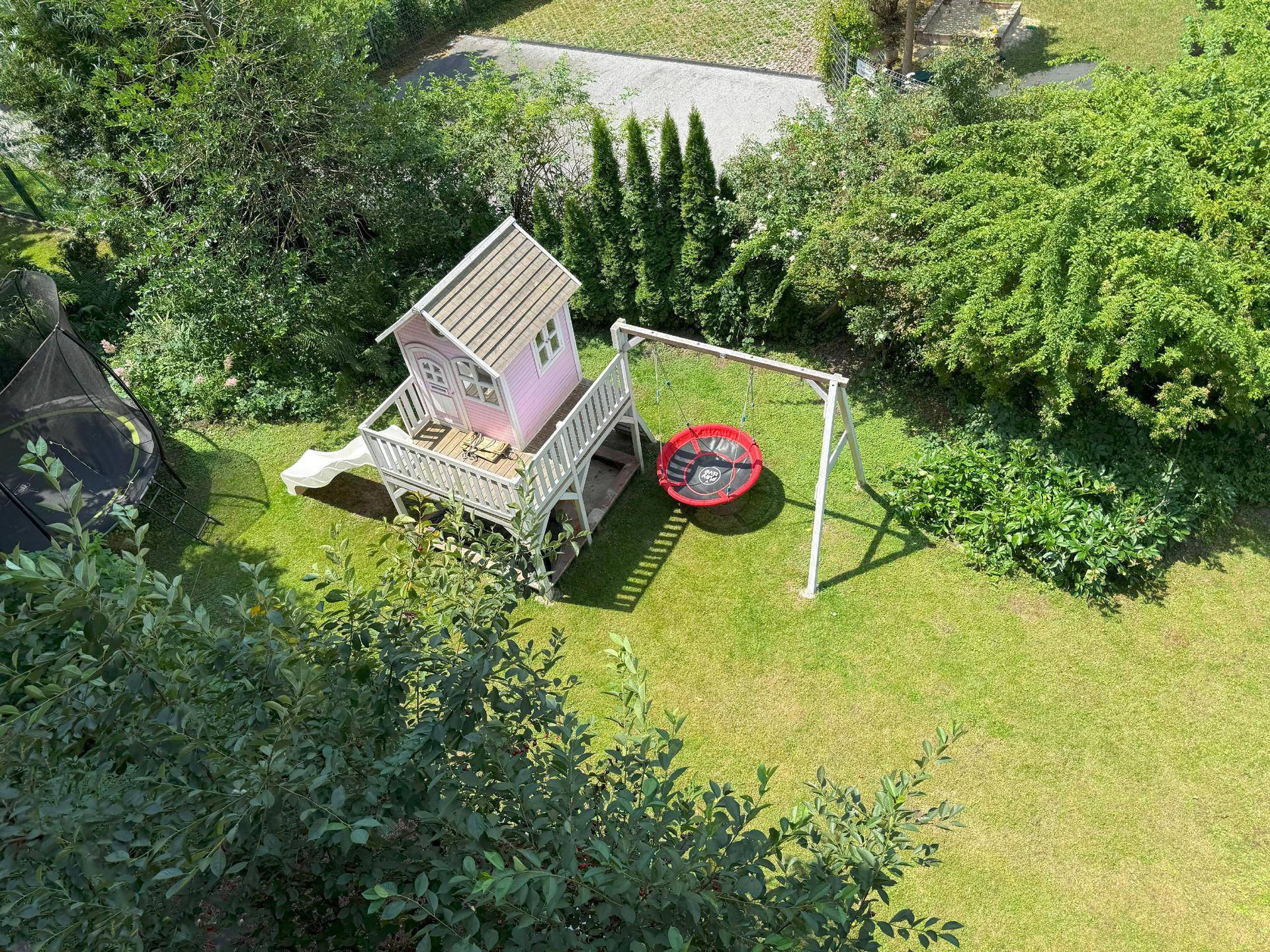 Gepflegter Gartenbereich mit Spielhaus, Schaukel und Trampolin für Kinder.