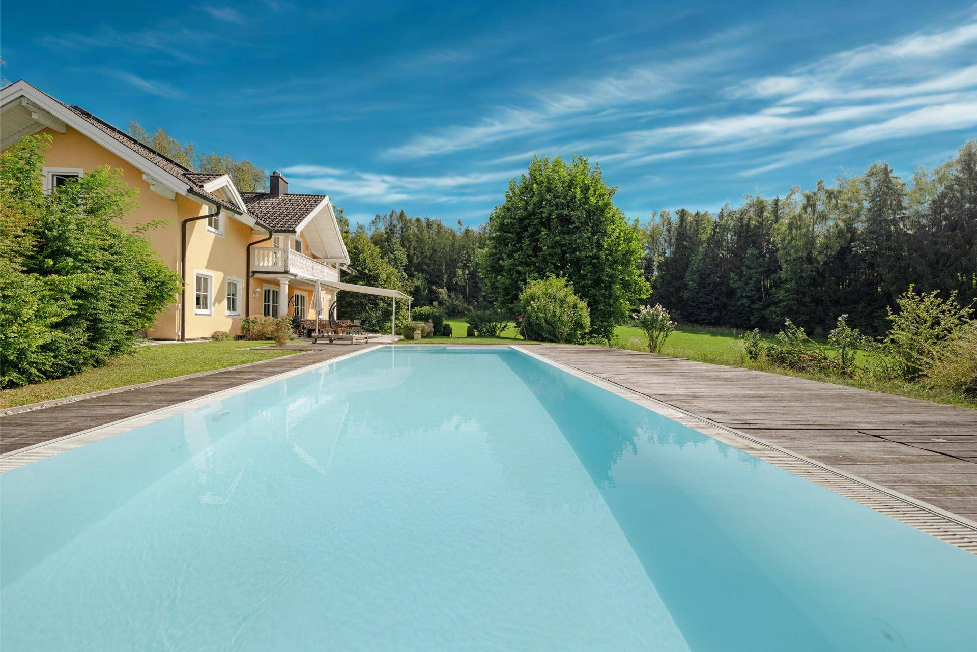 Blick auf das Landhaus mit großem Pool und Holzdeck unter blauem Himmel.