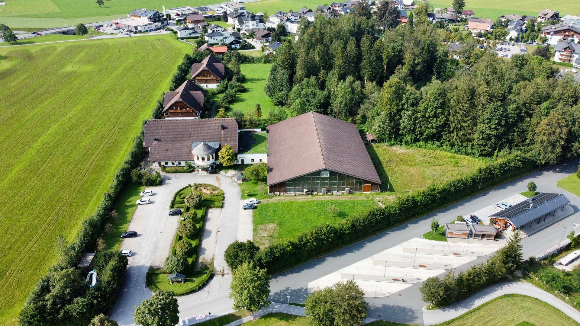 Gesamtanlage mit Hotelgebäude, großer Halle und weitläufigen Parkplätzen, umgeben von Natur.