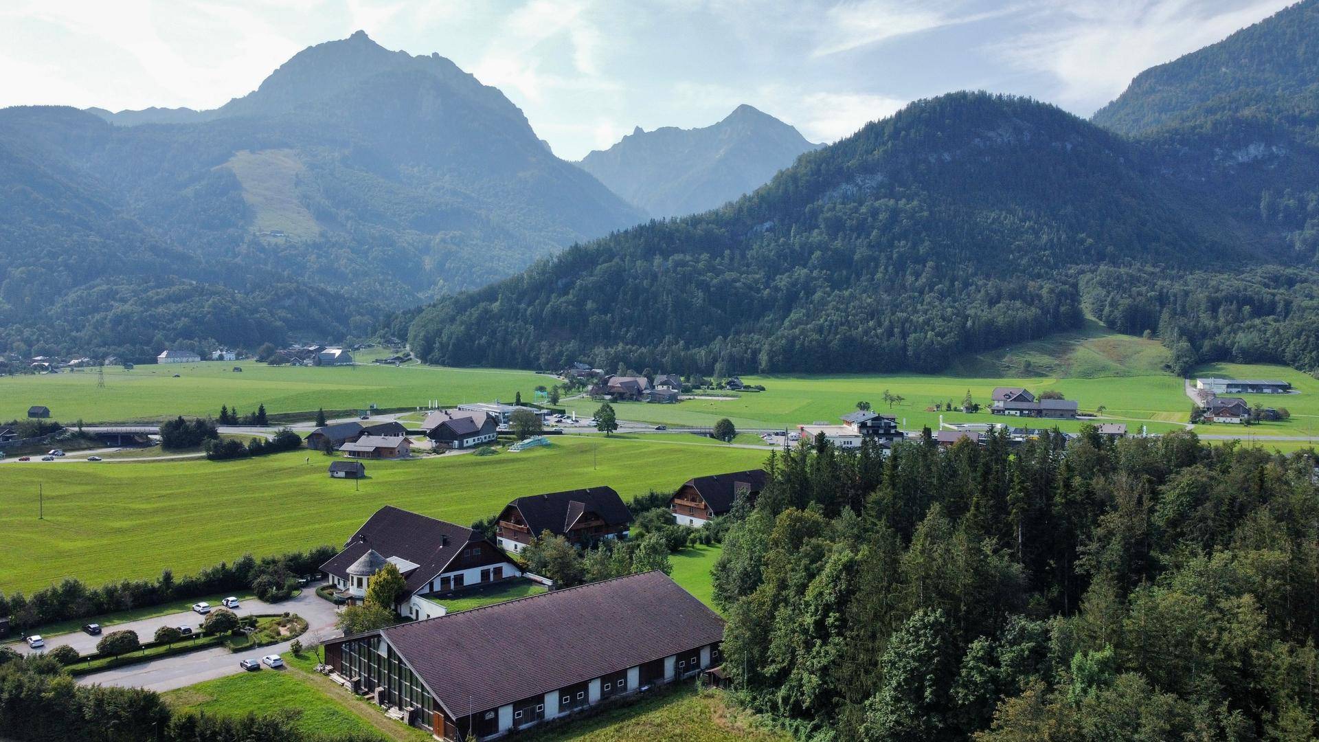 Weitläufige Anlage in einem grünen Tal, umgeben von Bergen und mit Blick auf eine nahegelegene Ortschaft.