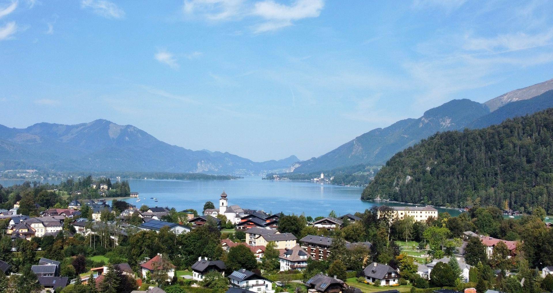 Weitläufiger Blick über eine charmante Ortschaft am Seeufer, eingebettet in eine beeindruckende Berglandschaft.