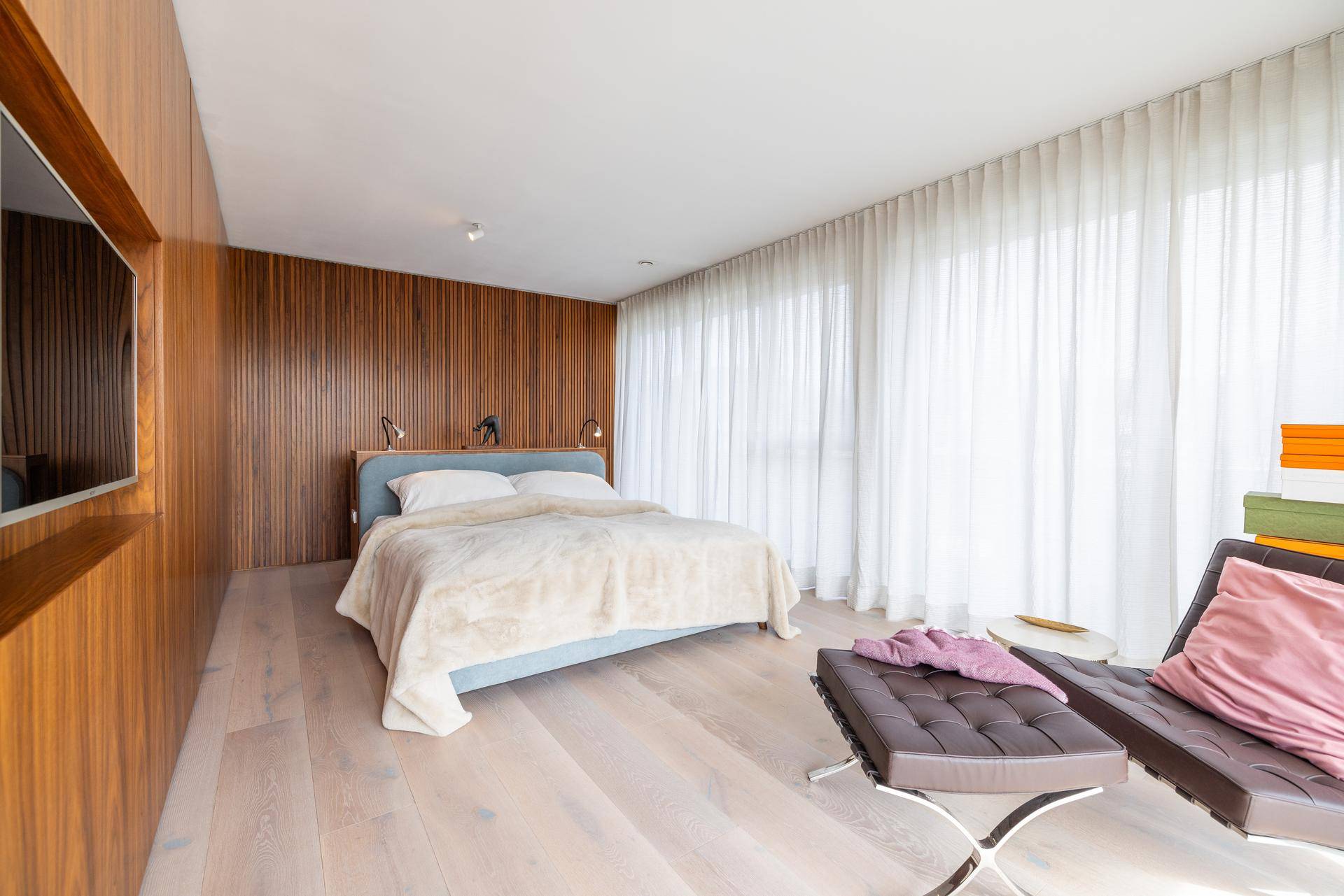 Modernes Schlafzimmer mit Holzwandverkleidung, großem Bett und bodentiefen Fenstern.