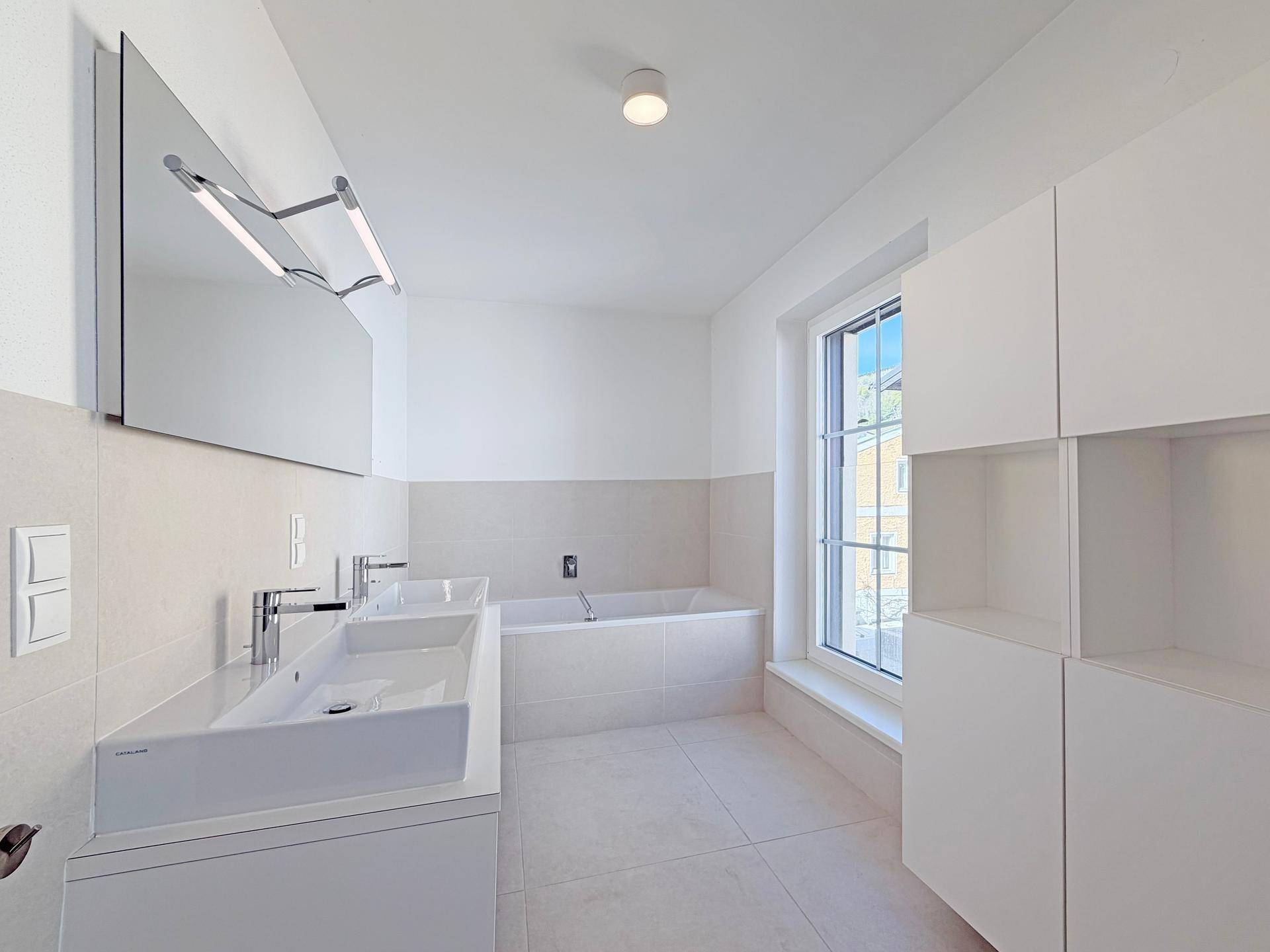 Helles, modernes Badezimmer mit Doppelwaschbecken, Badewanne und großem Fenster.