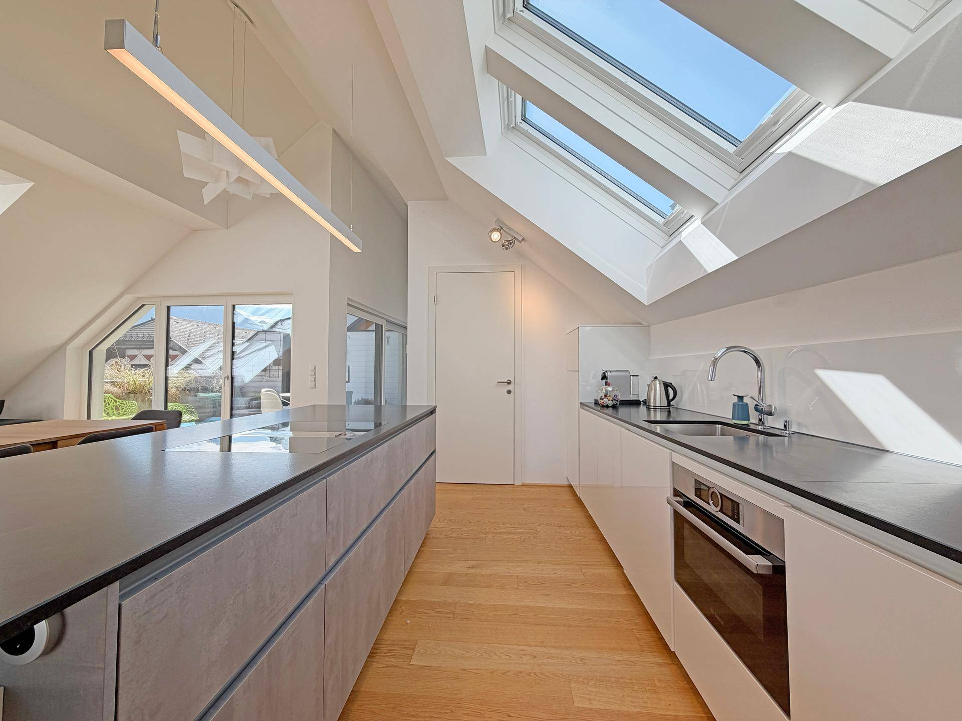 Moderne Einbauküche mit Kücheninsel, integriertem Backofen und viel Tageslicht durch Dachfenster.