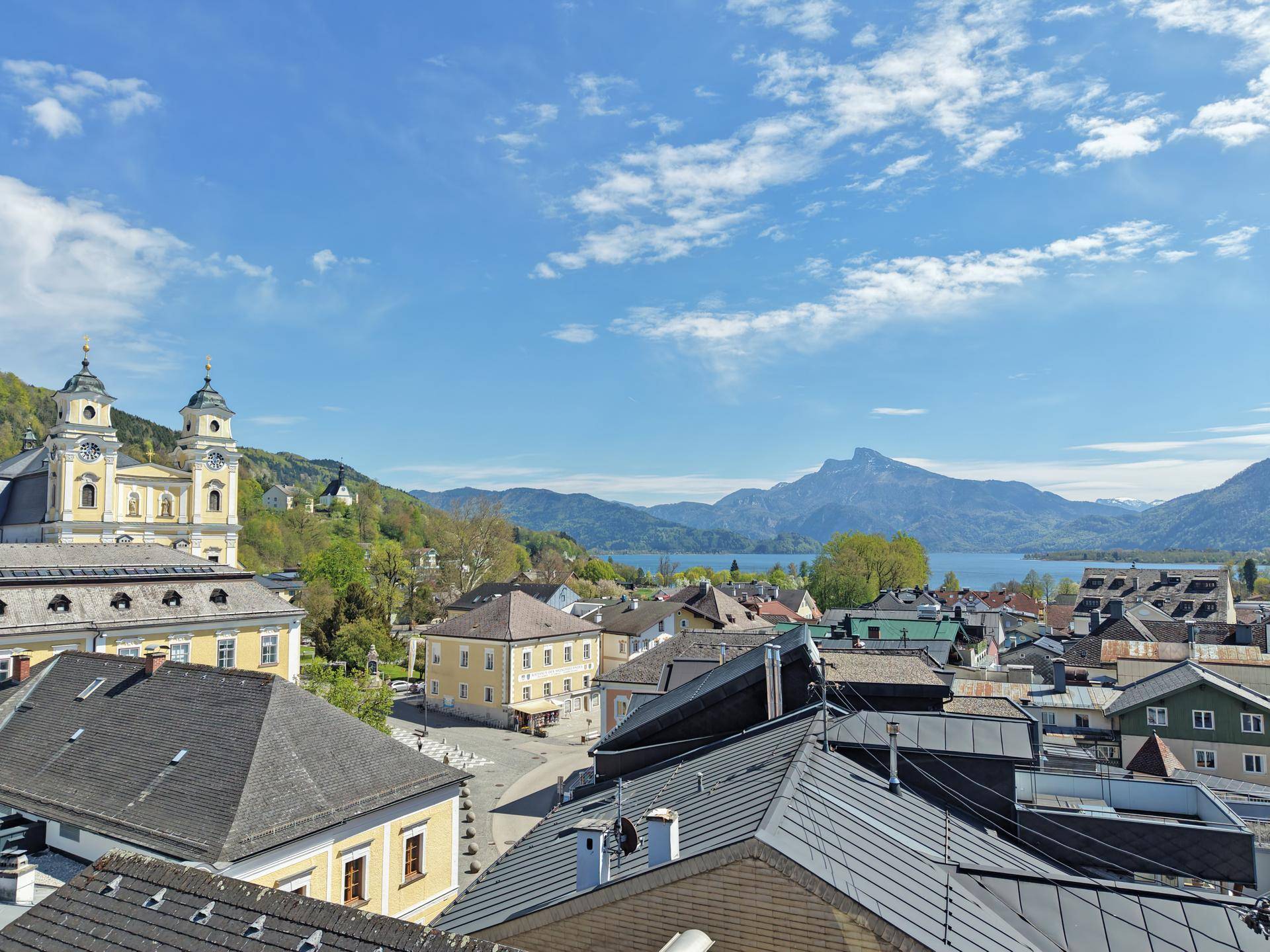 Panoramablick über eine malerische Stadt mit See und Bergen im Hintergrund.