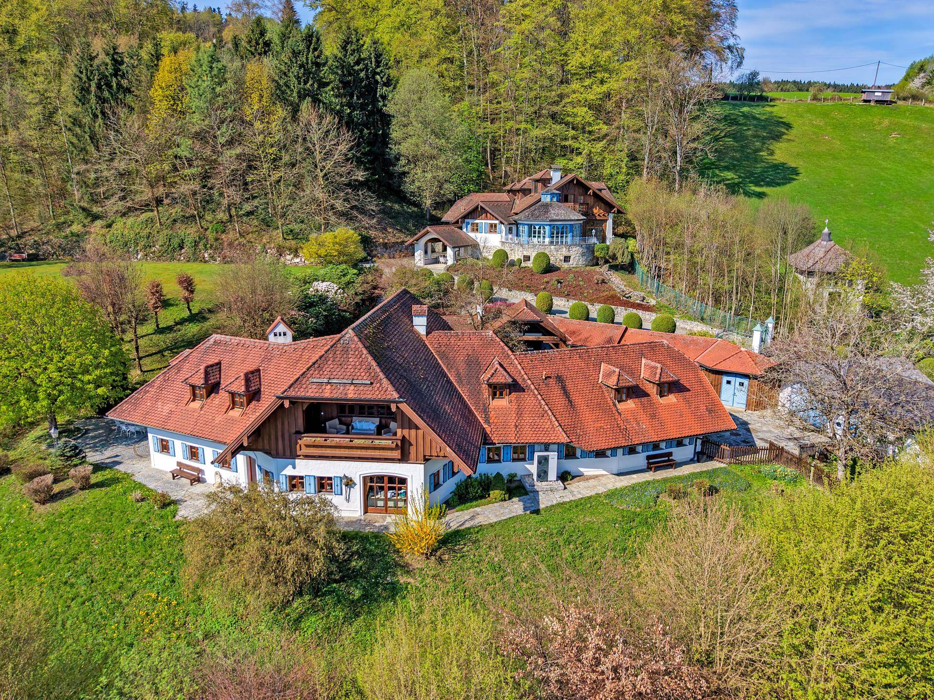 Malerisches Anwesen mit mehreren Gebäuden, umgeben von grünen Hügeln und Wäldern.