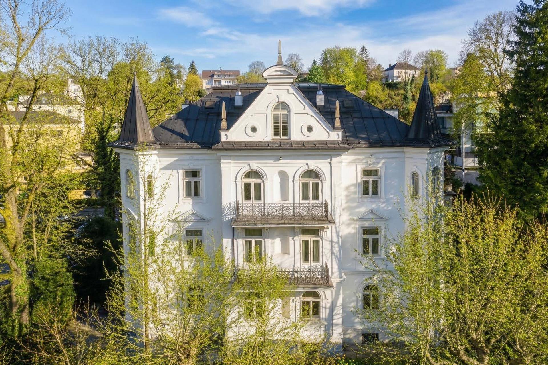 Frontansicht der prächtigen weißen Villa mit markanten Türmchen und gepflegter Umgebung.