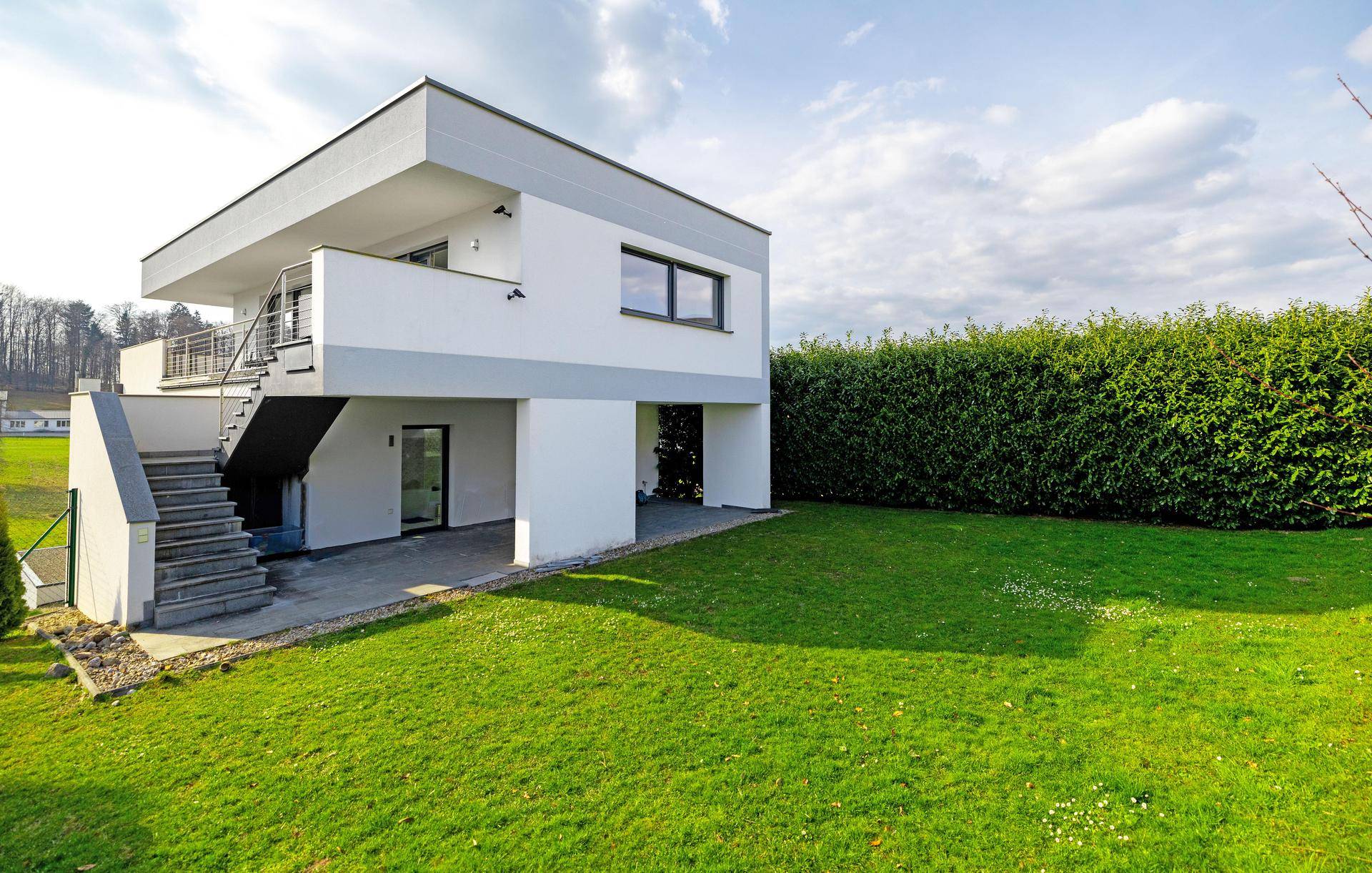 Modernes Haus mit gepflegtem Rasen, hoher Hecke und Außentreppe zu den oberen Etagen.