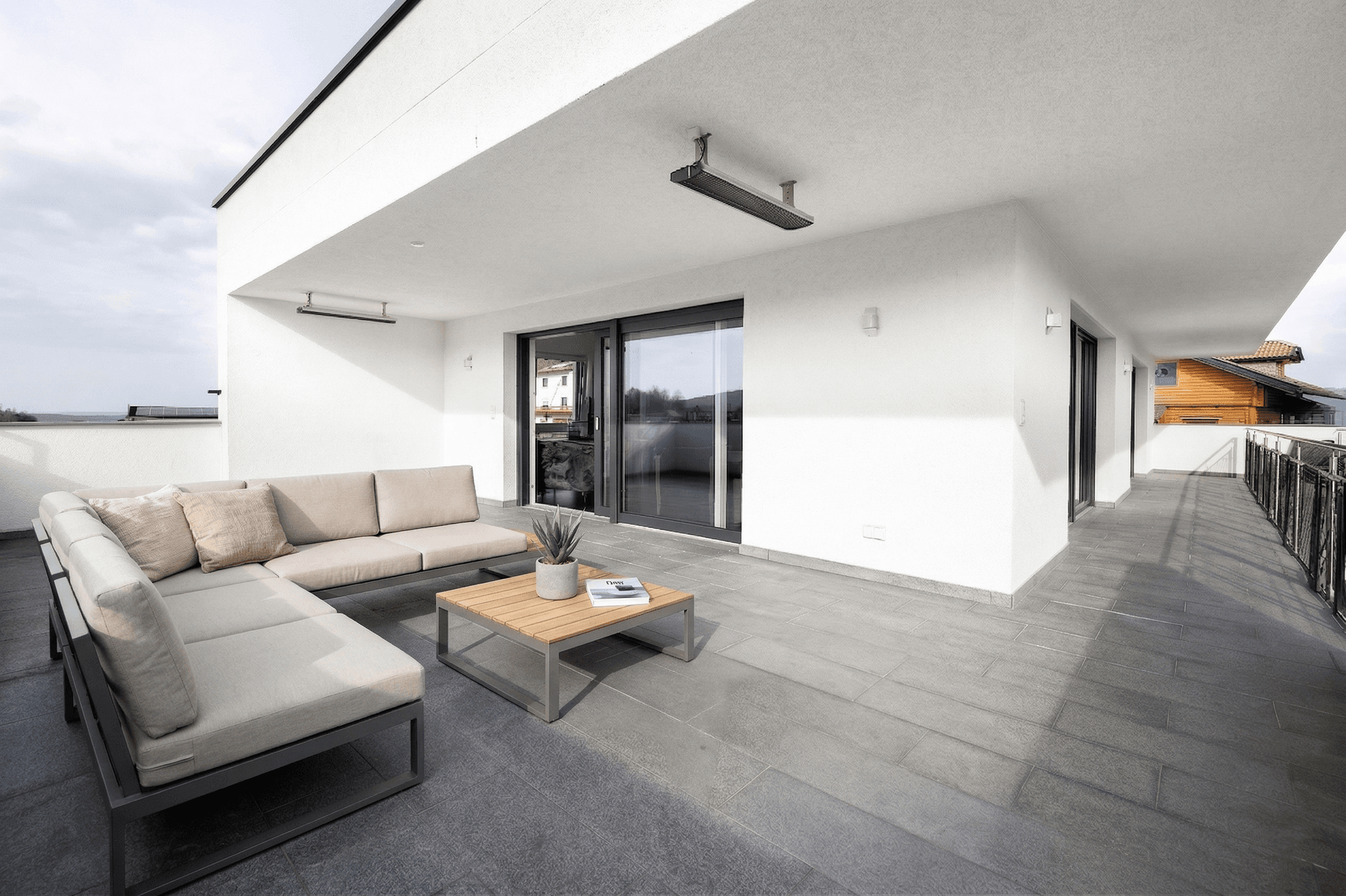 Geräumige Terrasse mit modernen Lounge-Möbeln, Fliesenboden und Blick auf die Umgebung.