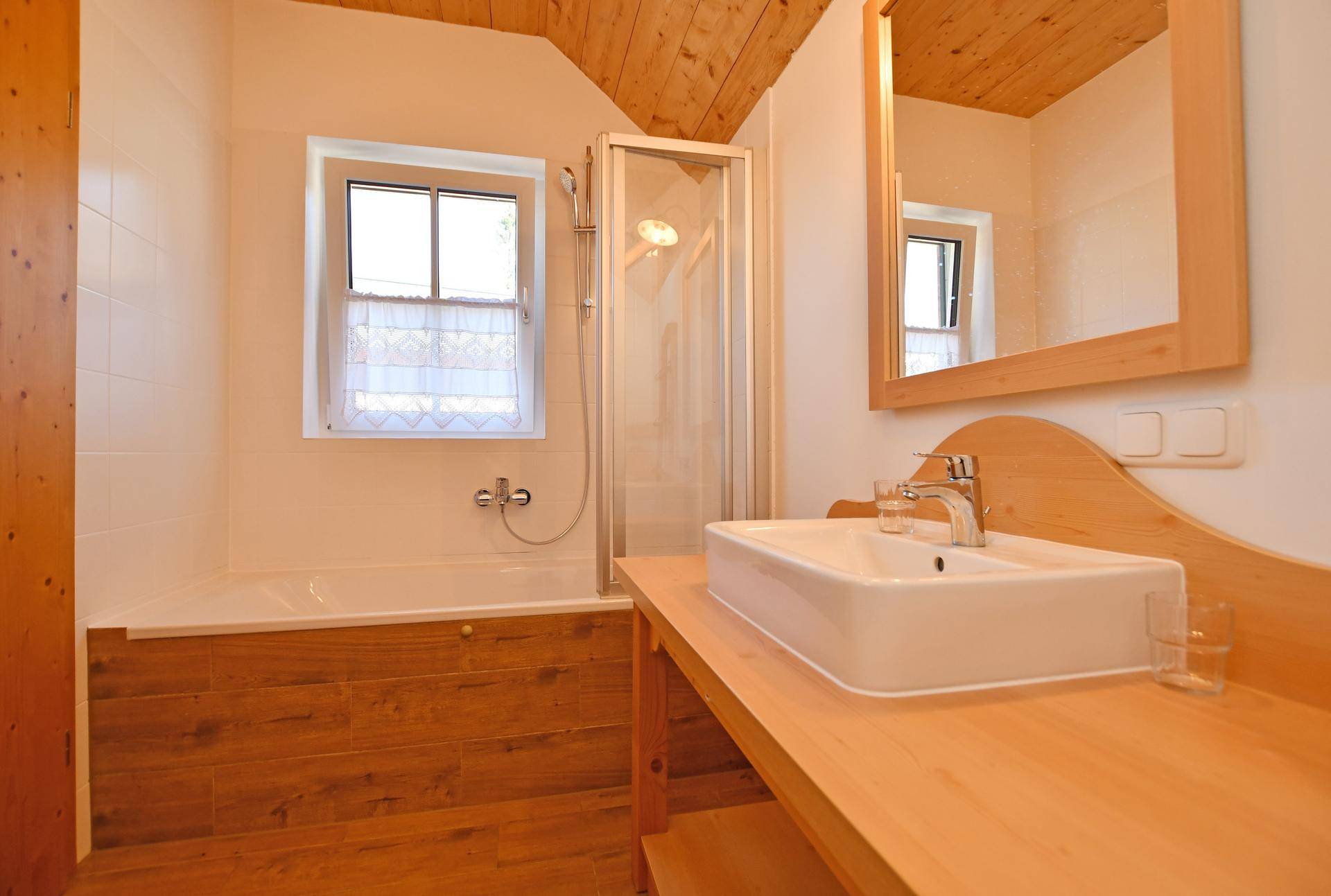 Badezimmer mit Badewanne, Duschkabine, Einzelwaschbecken und einem Fenster für natürliches Licht.