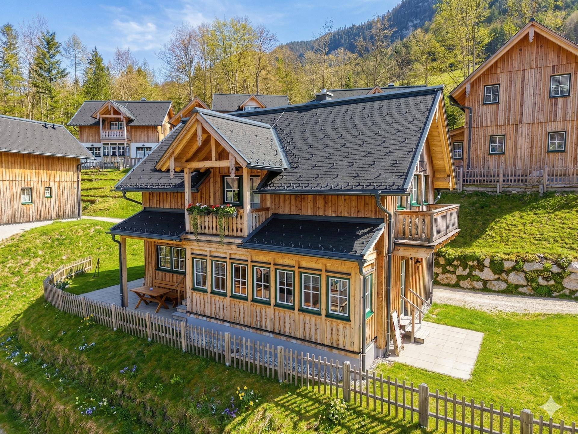 Attraktives Holzchalet mit dunklem Dach und Balkon, umgeben von grünen Wiesen in den Bergen.