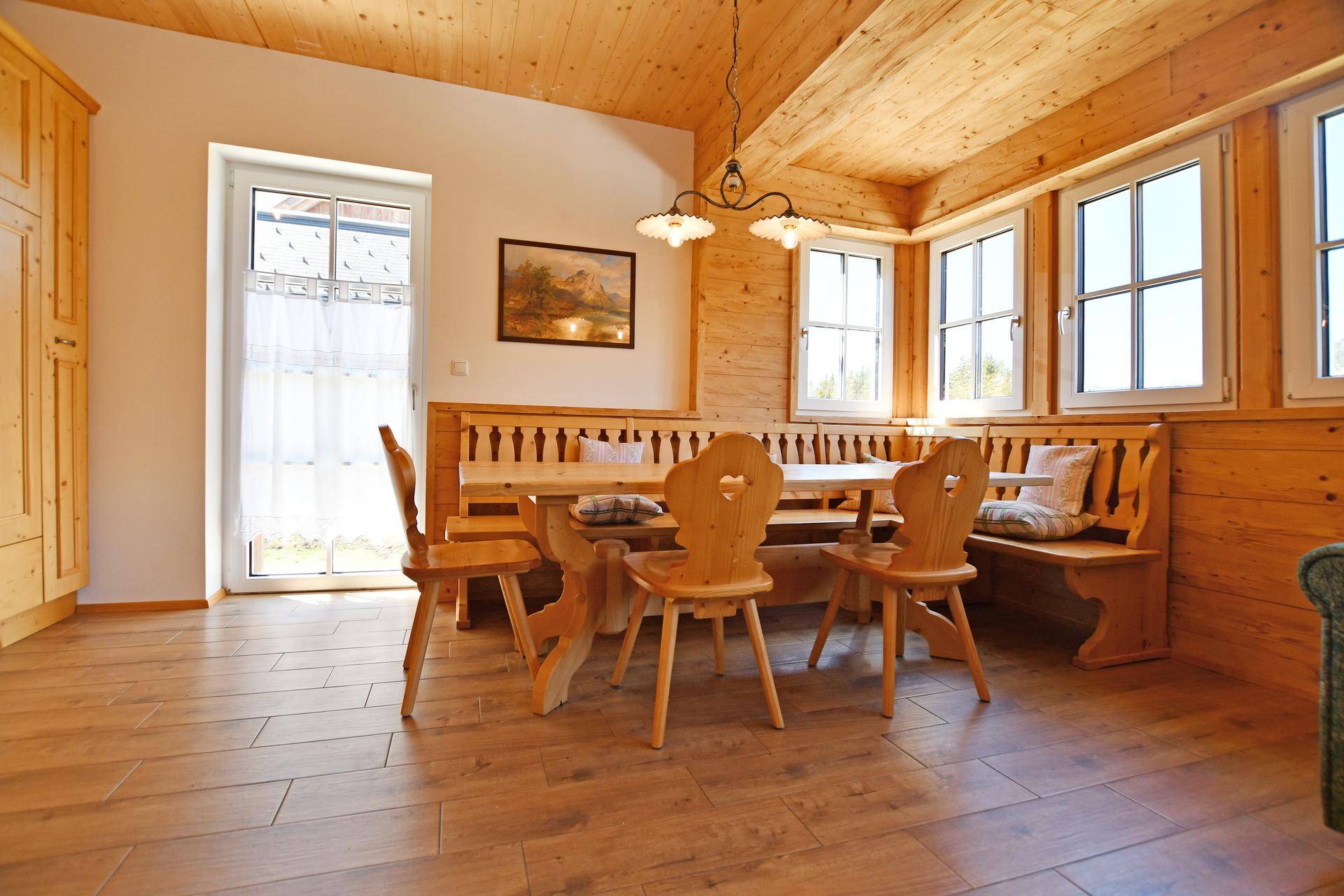 Rustikaler Essbereich mit Holztisch und Bänken, umgeben von Holzwänden und mit Zugang nach draußen.