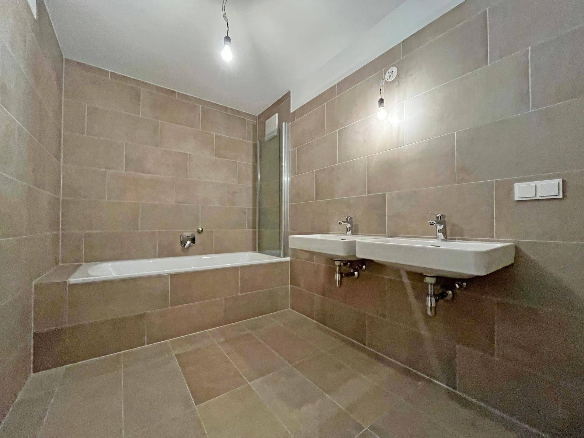 Modernes Badezimmer mit Doppelwaschbecken, Badewanne und braunen Wand- und Bodenfliesen.