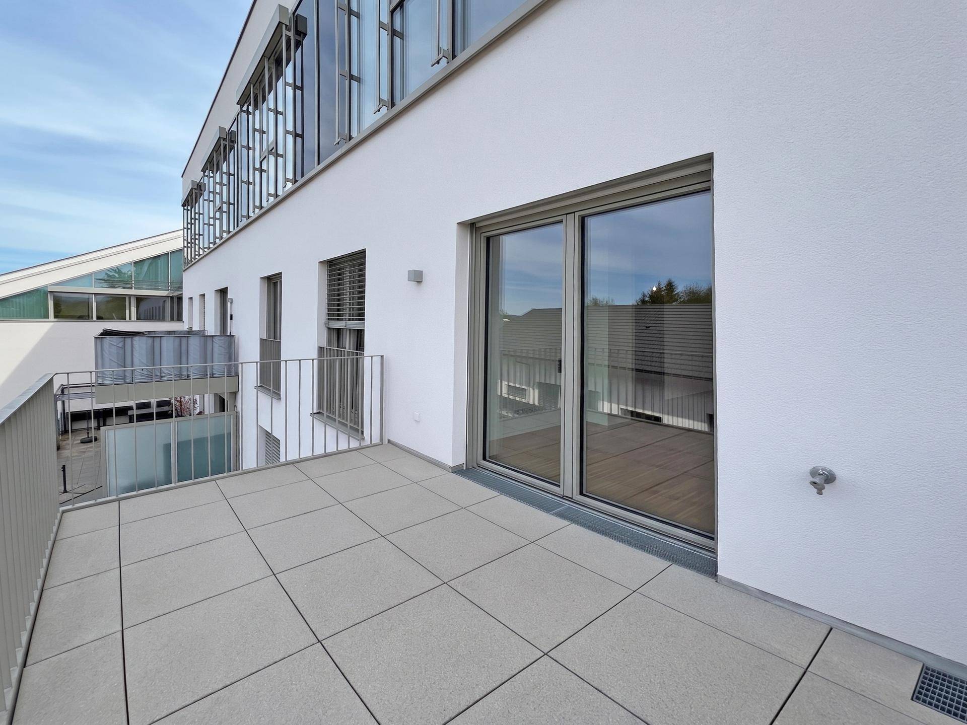 Geräumiger Balkon mit Fliesenboden und Blick auf die umliegenden Gebäude und den Himmel.