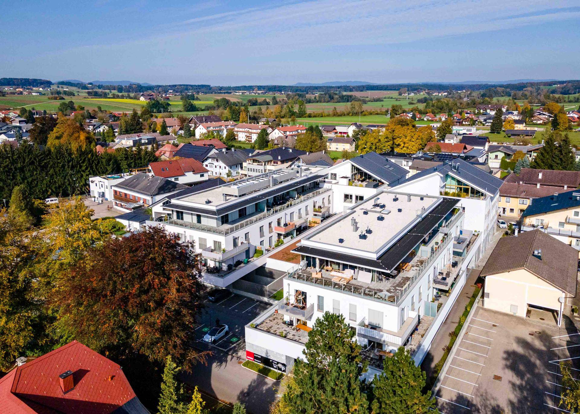 Luftaufnahme einer modernen Wohnanlage mit Flachdächern und Photovoltaikanlagen in ländlicher Umgebung.