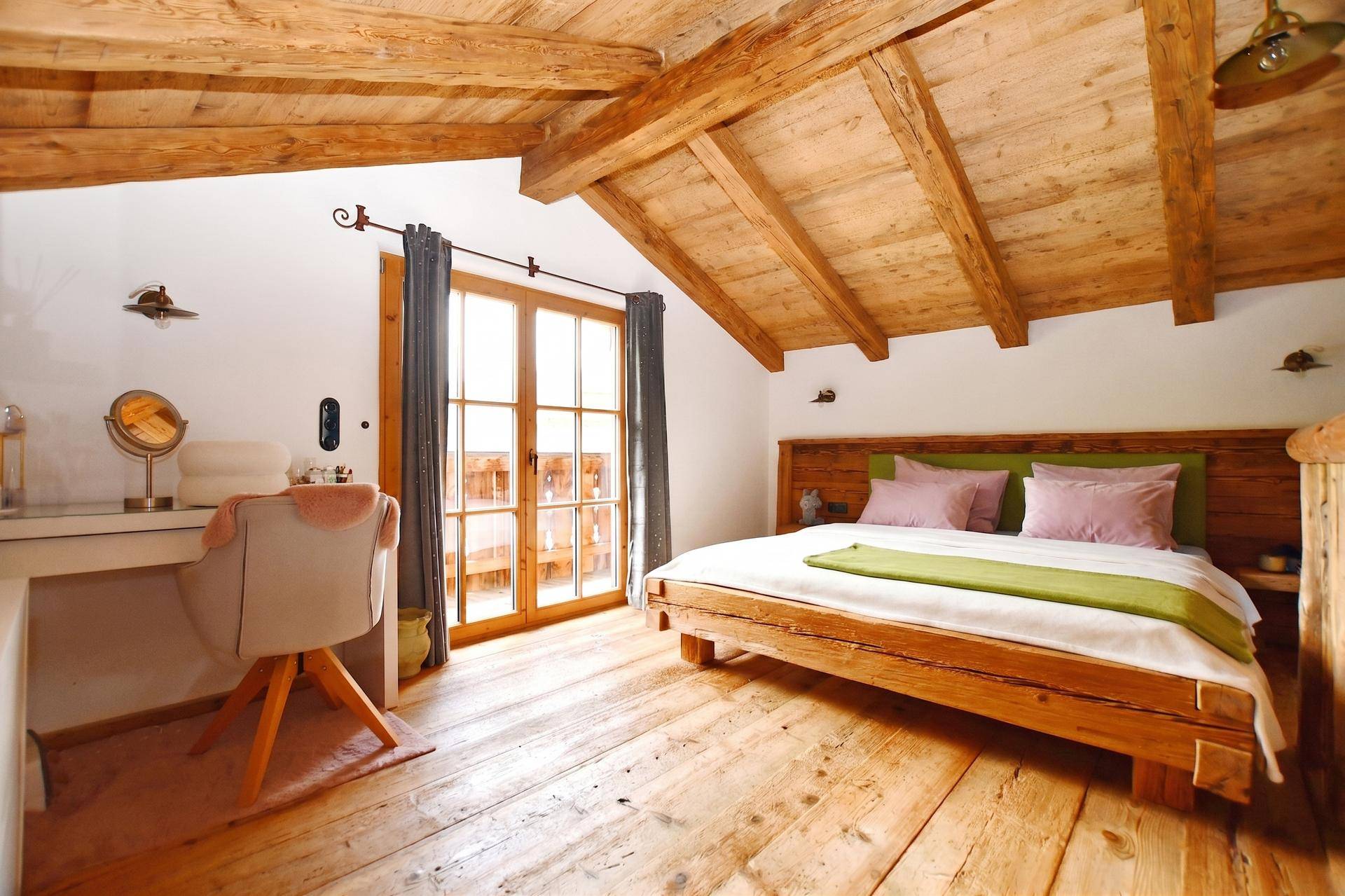 Helles Schlafzimmer mit Holzbalkendecke, Dielenboden und Zugang zu einem Balkon.