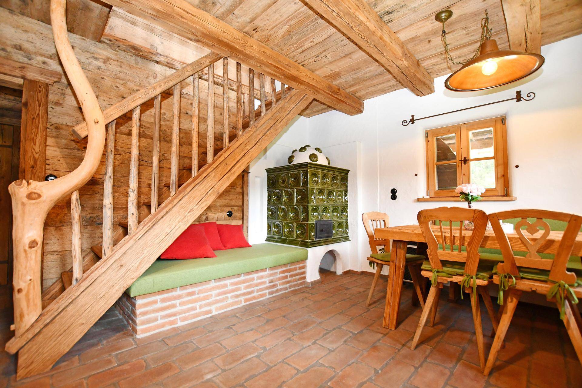 Gemütlicher Essbereich mit traditionellem Kachelofen, Holztreppe und Terrakottaboden.