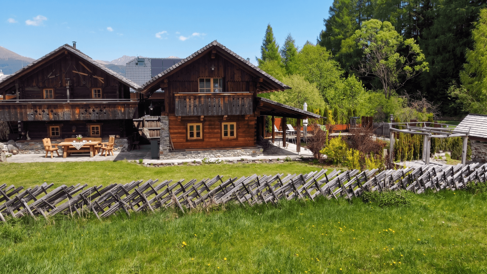 Charmantes Holzchalet mit traditionellem Holzzaun und weitläufiger grüner Wiese im Vordergrund.