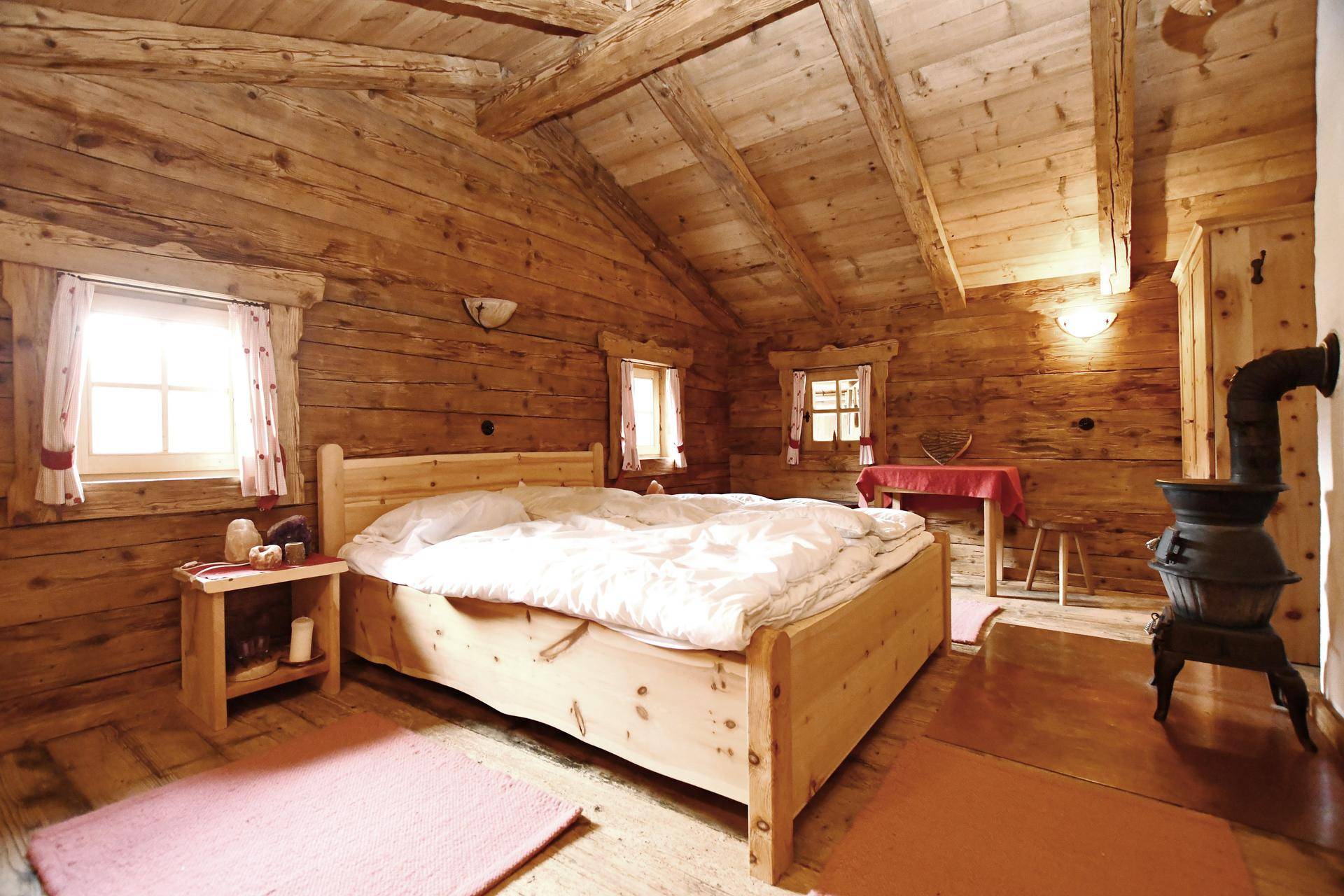 Gemütliches Schlafzimmer mit Holztäfelung, Dielenboden und einem traditionellen Holzofen.