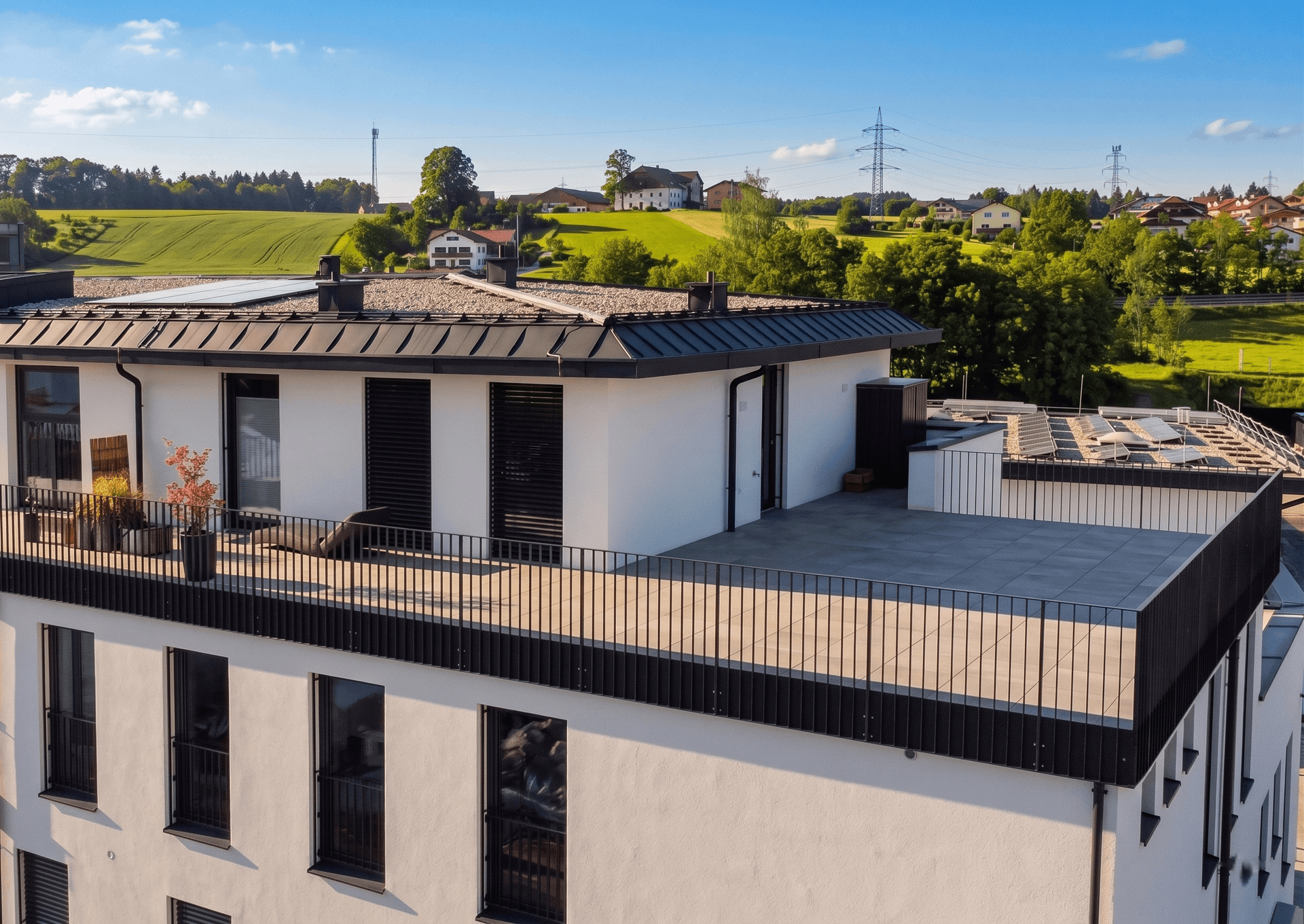 Moderner Neubau mit großer Dachterrasse und Blick auf grüne Felder und die umliegende Landschaft.