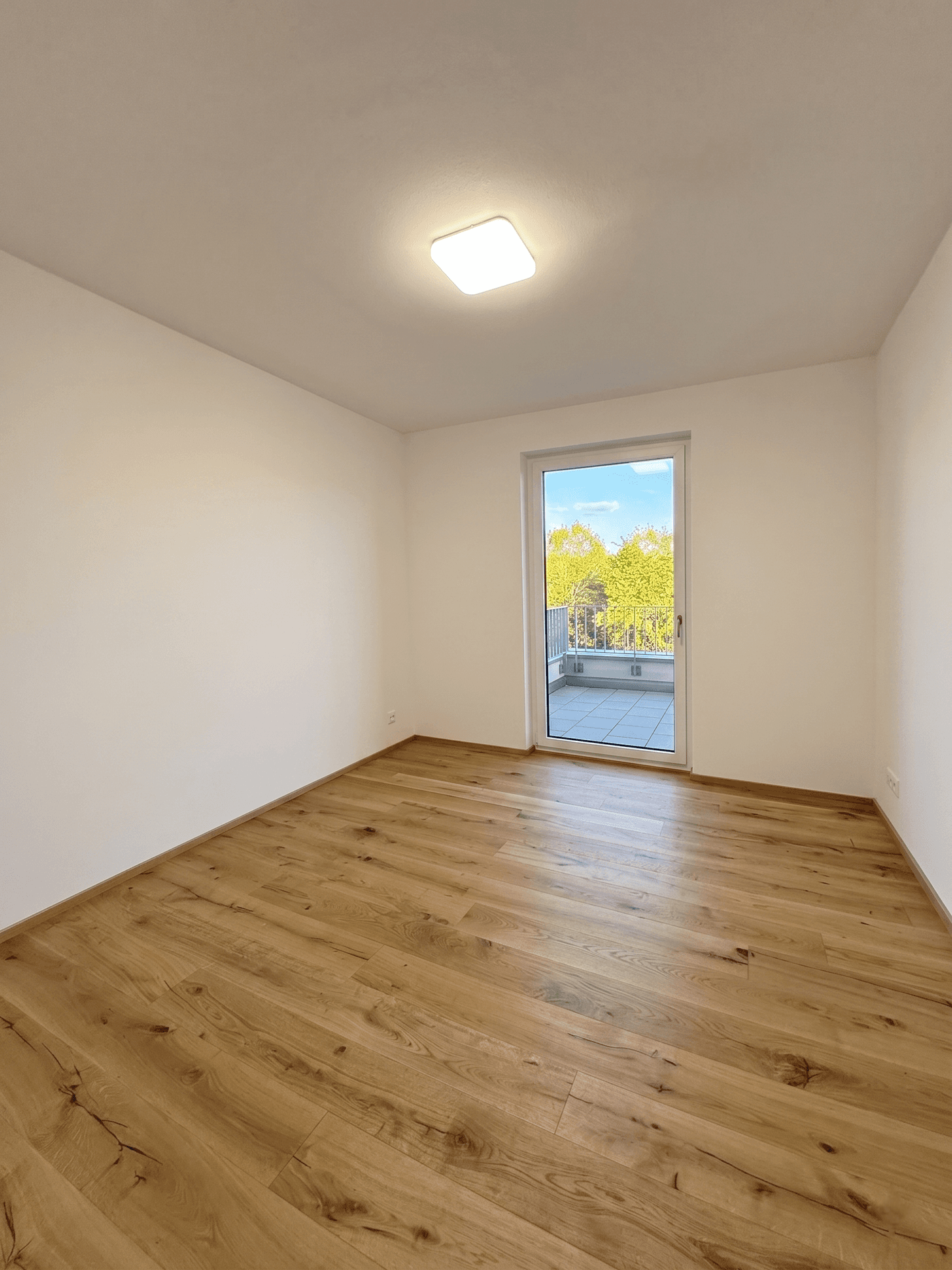Leerer Raum mit Holzboden und Zugang zu einem Balkon oder einer kleinen Terrasse.