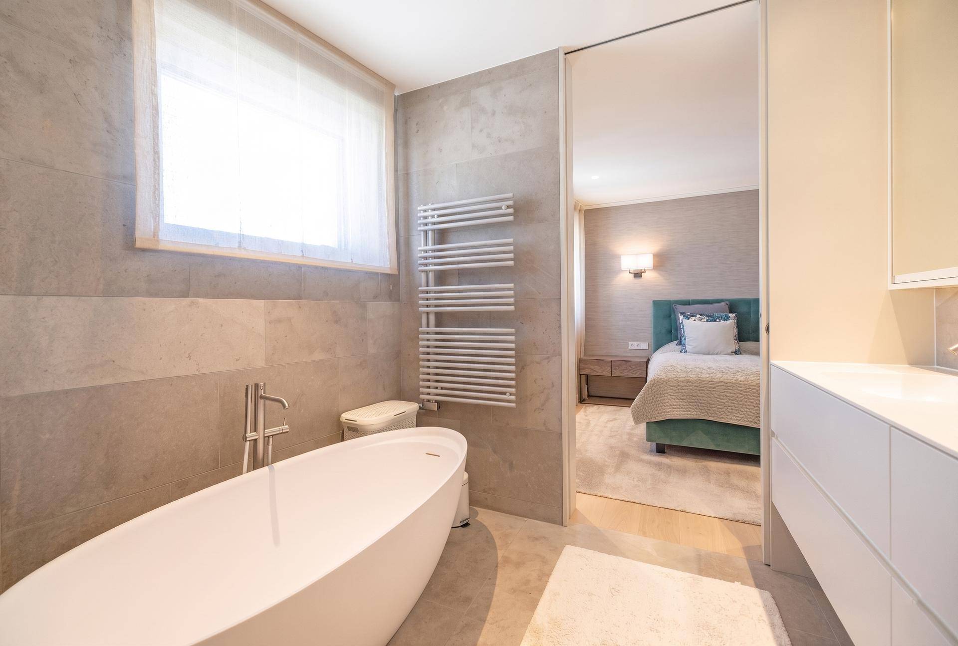 Elegantes Badezimmer mit freistehender Badewanne, modernen Fliesen und Zugang zum Schlafzimmer.