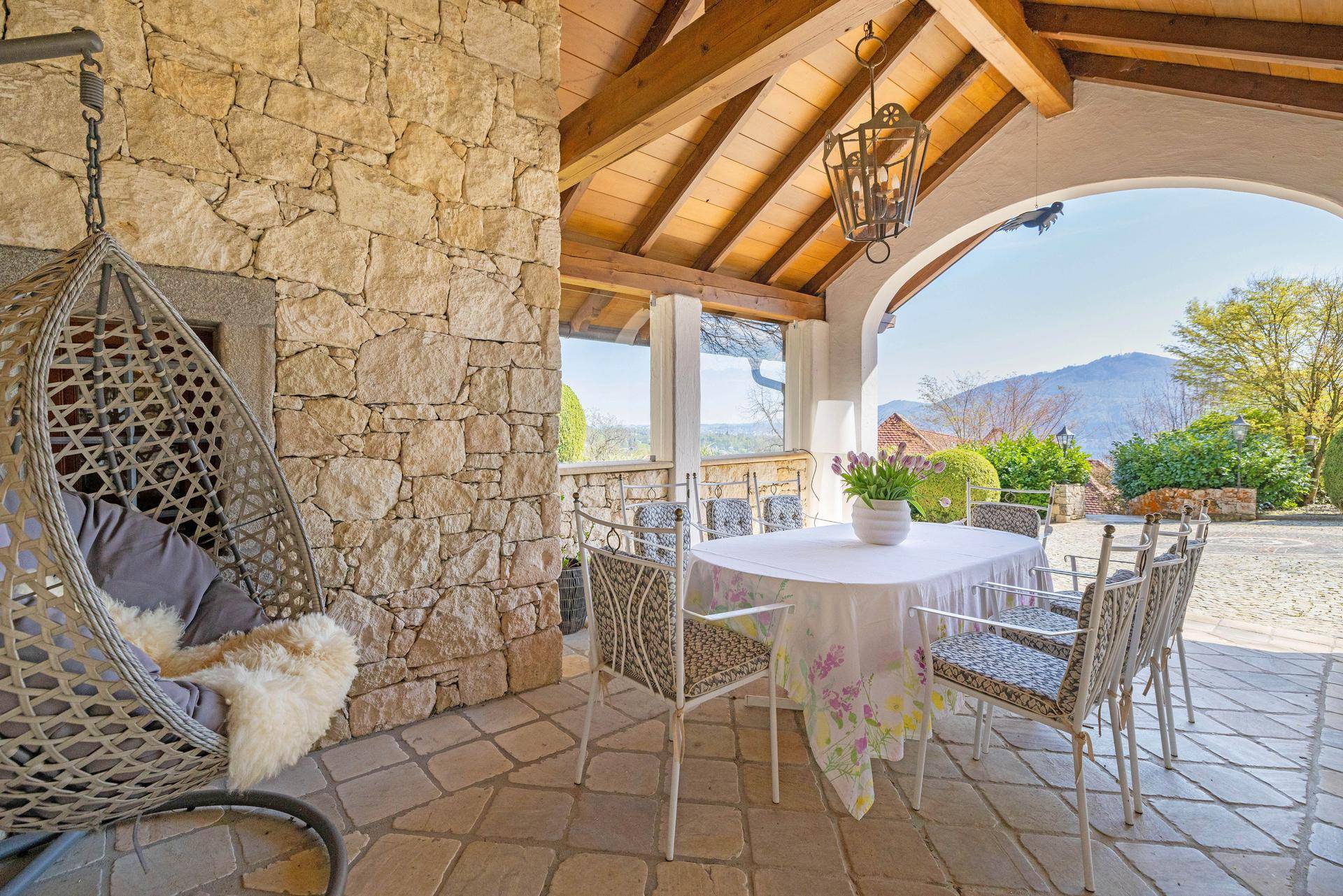 Überdachte Terrasse mit Steinfliesen, rustikalen Holzbalken und gemütlichen Sitzgelegenheiten im Freien.