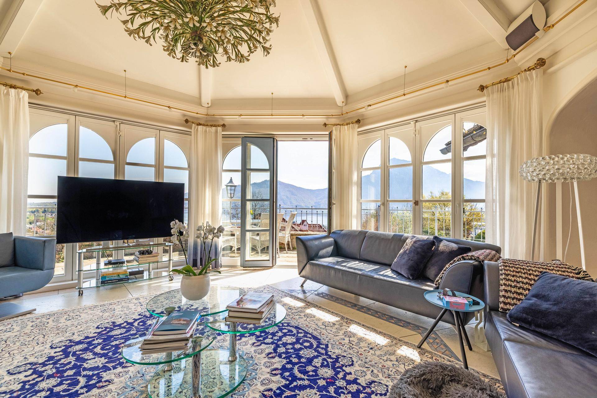 Elegantes Wohnzimmer mit großen Rundbogenfenstern, Seeblick und Zugang zu einem Balkon.