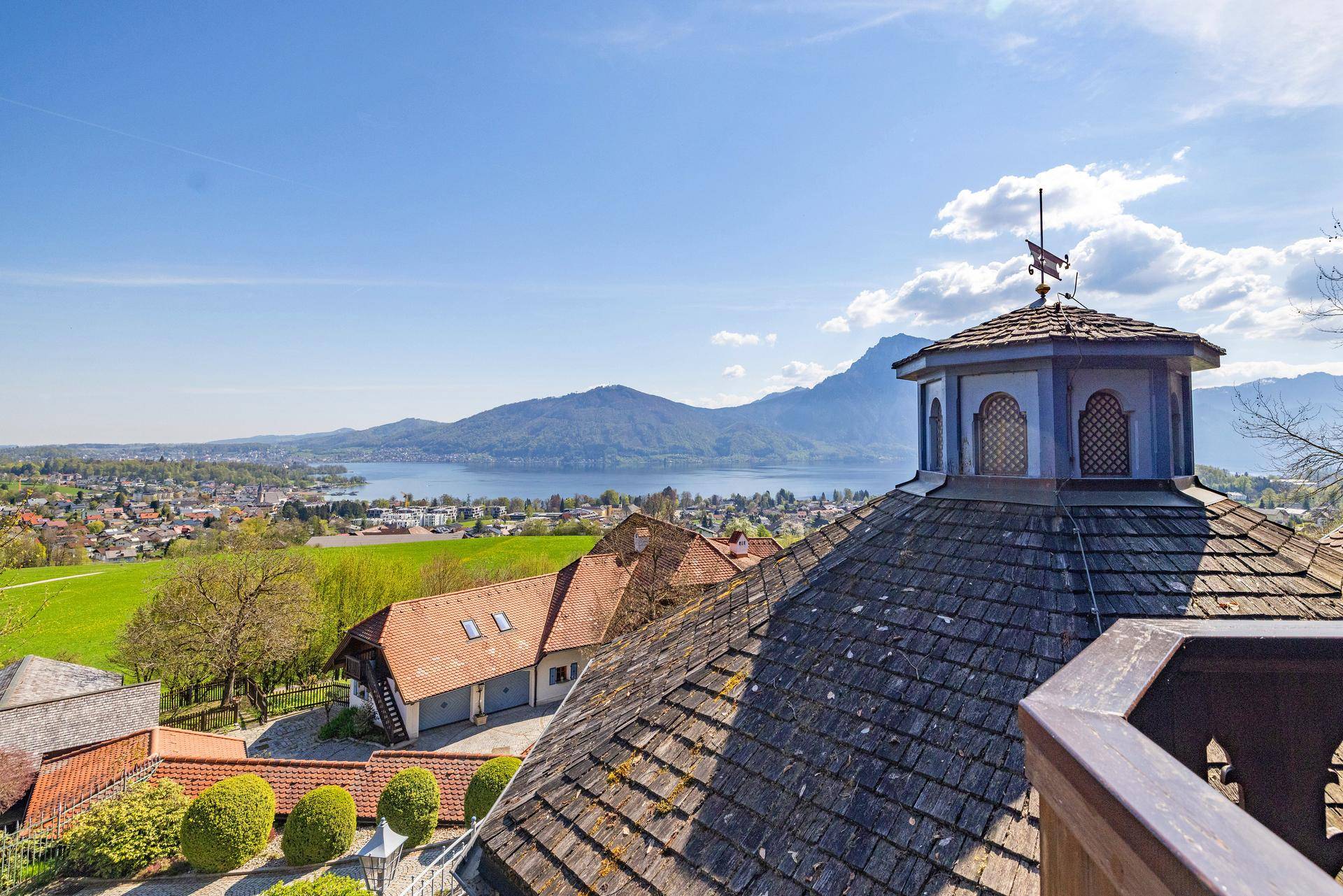 Historisches Dach mit Wetterfahne und weitem Blick über den See und die umliegende Landschaft.