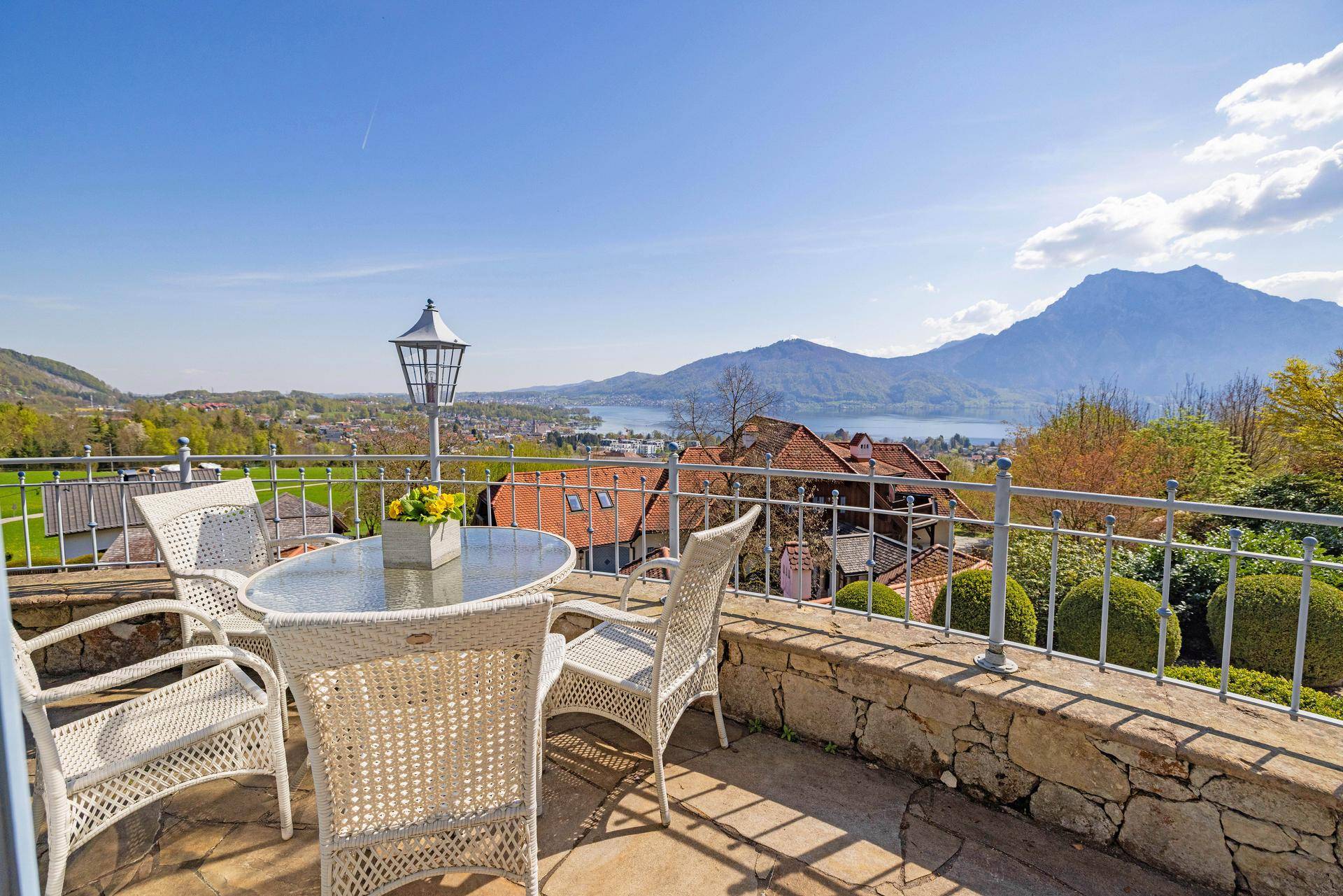 Gemütlicher Balkon mit Korbmöbeln und einem weiten Panoramablick auf den See und die Berge.