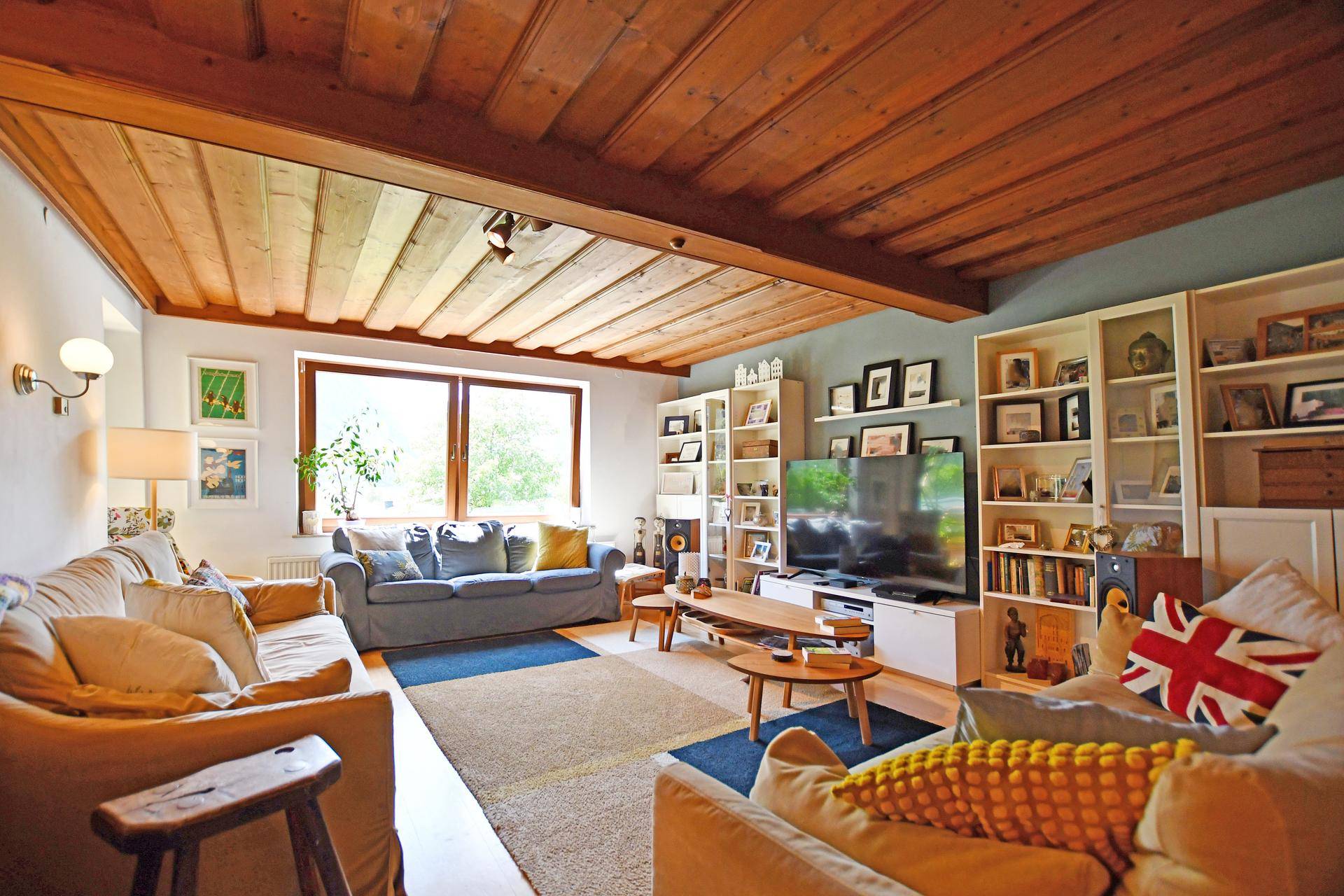 Gemütliches Wohnzimmer mit Holzbalkendecke, bequemen Sofas und Blick ins Grüne.