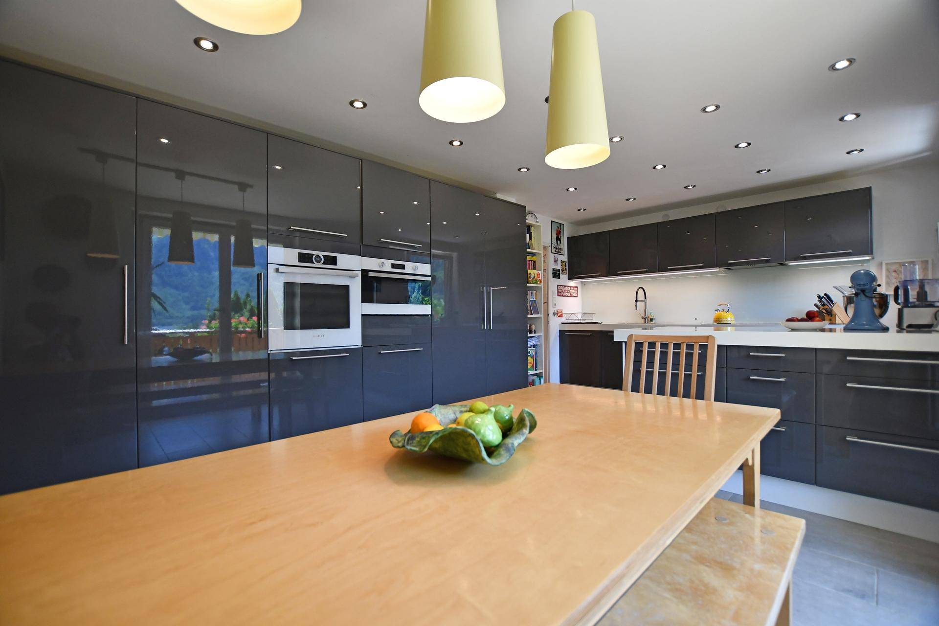 Moderne Küche mit glänzenden grauen Schränken, integrierten Geräten und Holztisch.