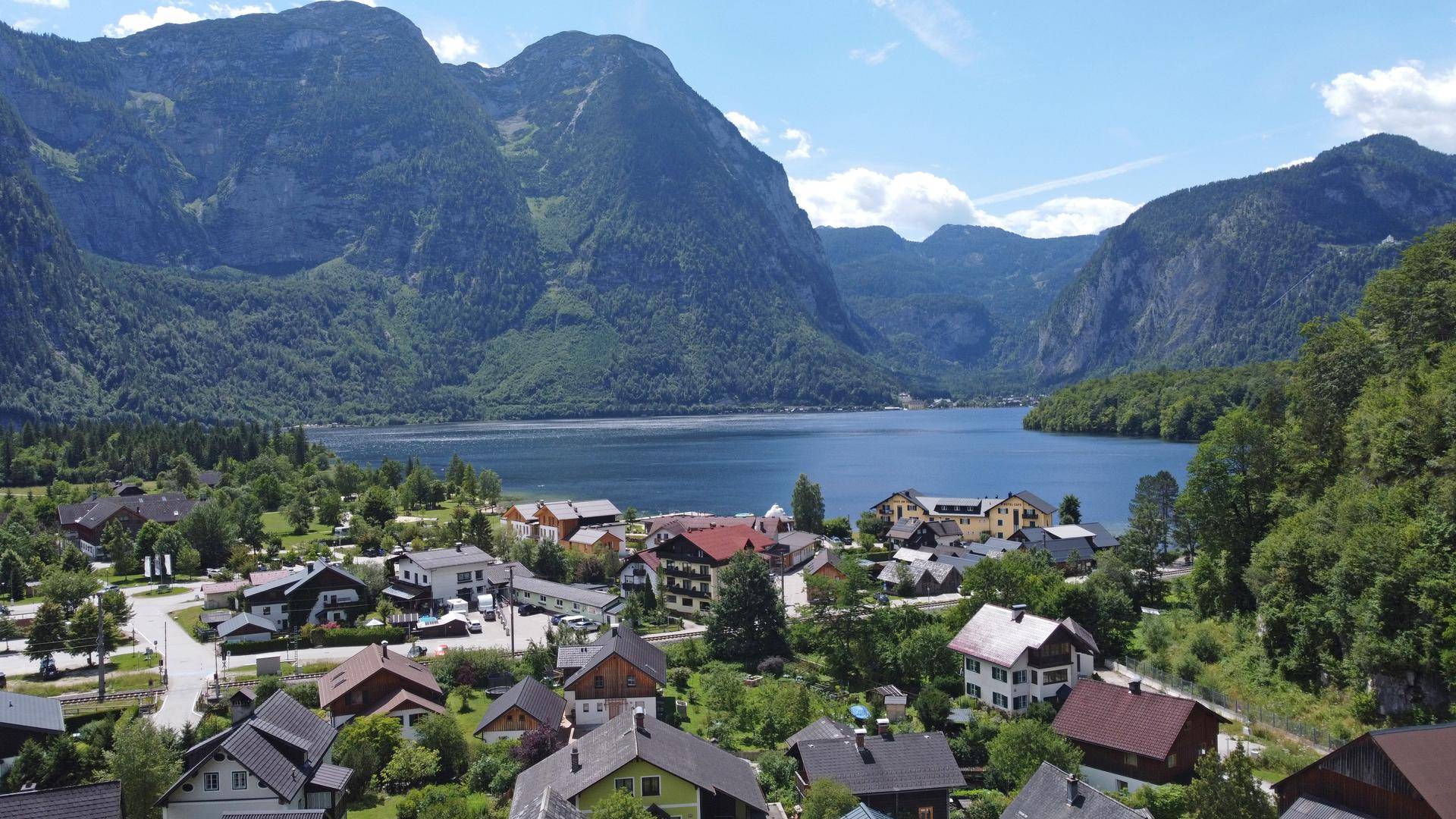 Malerische Ansicht eines Dorfes am Seeufer, umgeben von majestätischen Bergen unter blauem Himmel.