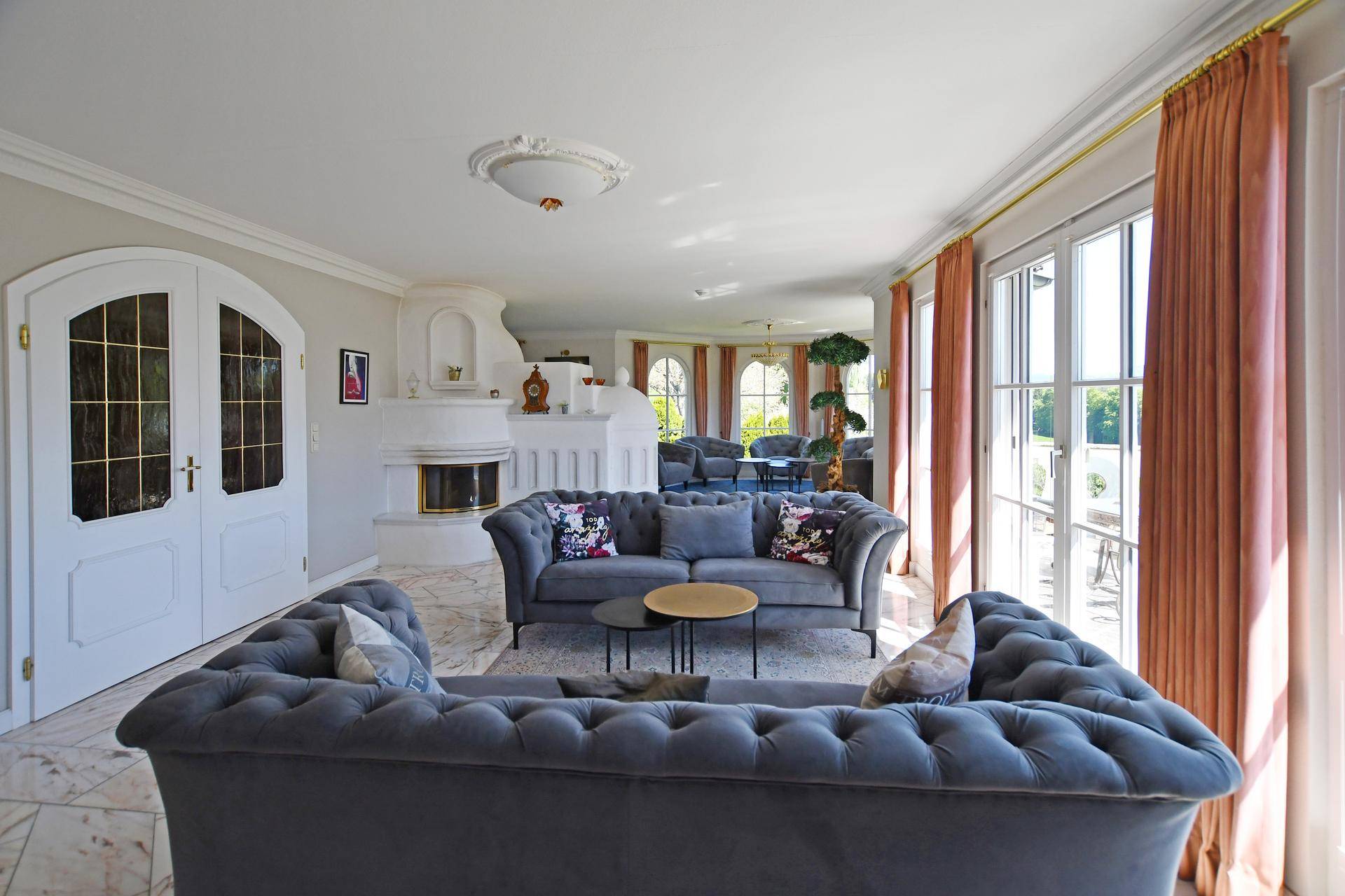 Geräumiges Wohnzimmer mit Chesterfield-Sofas, Kamin und Zugang zur Terrasse.