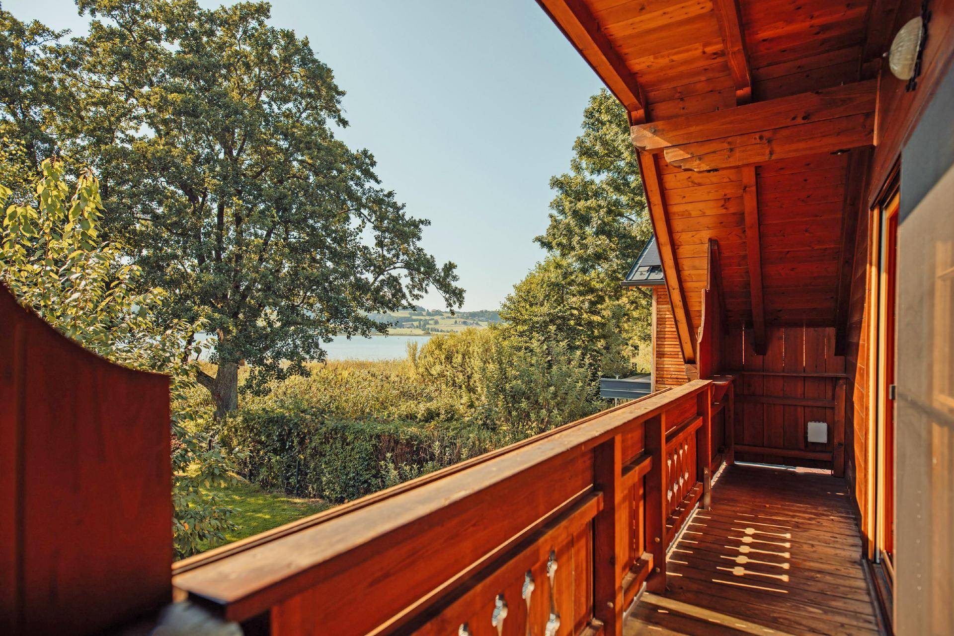 Holzbalkon mit kunstvollem Geländer bietet einen weiten Blick auf den See und die umliegende Natur.
