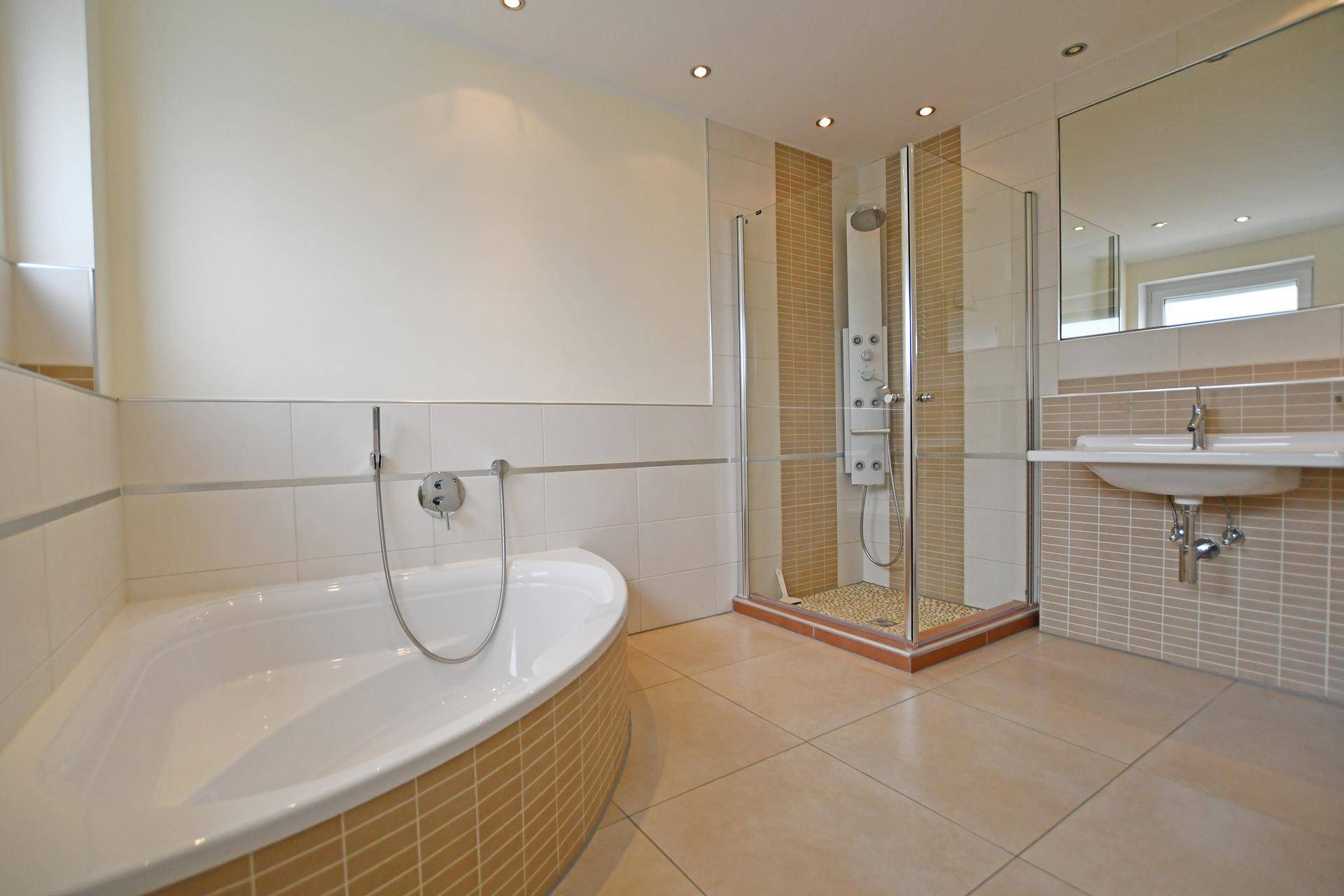 Modernes Badezimmer mit Badewanne, Duschkabine und beigen Fliesen an Wänden und Boden.