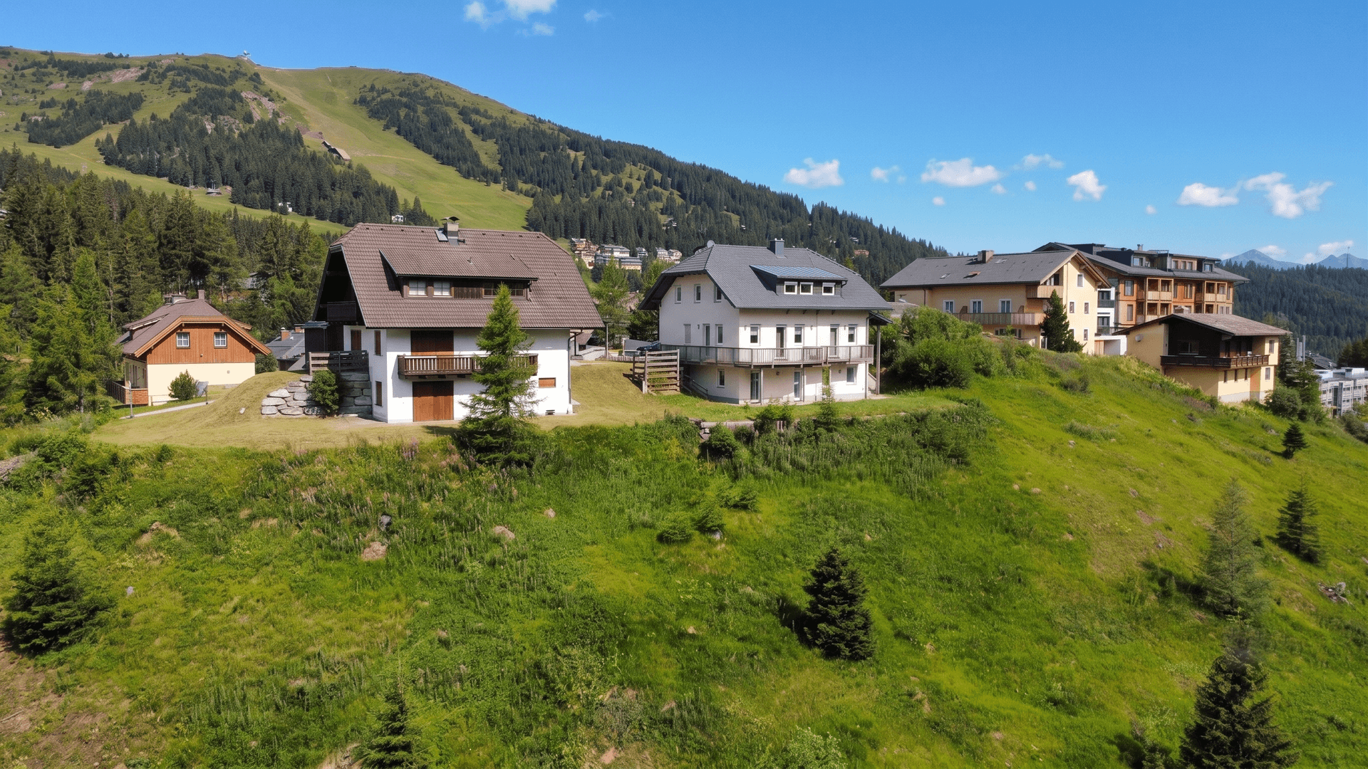 Mehrere Häuser in einer malerischen Berglandschaft mit grünen Hängen unter blauem Himmel.
