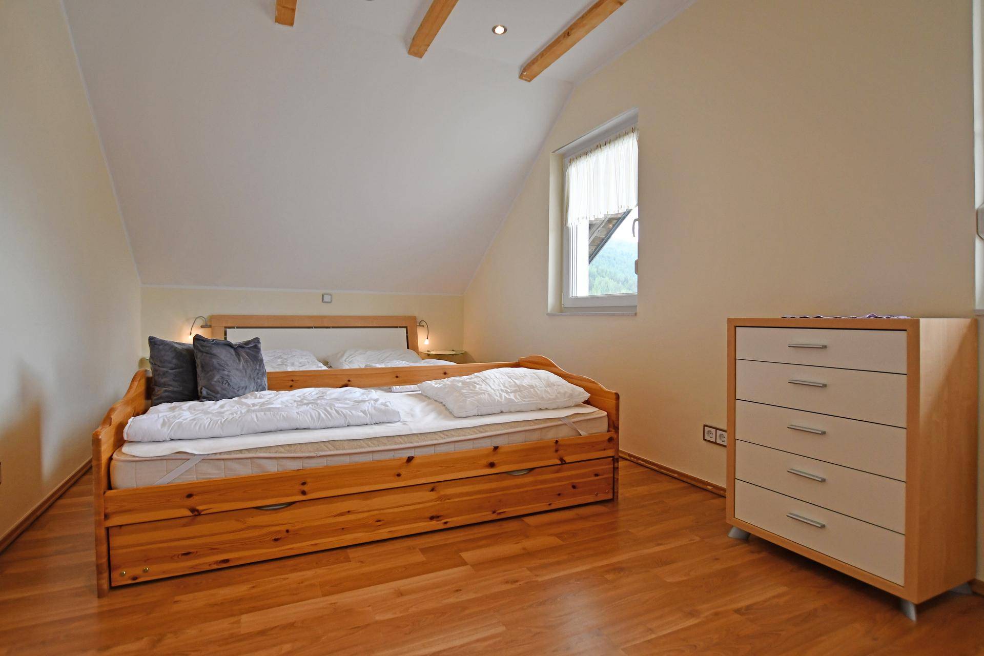 Gemütliches Schlafzimmer mit Holzboden, Dachschräge und sichtbaren Holzbalken an der Decke.