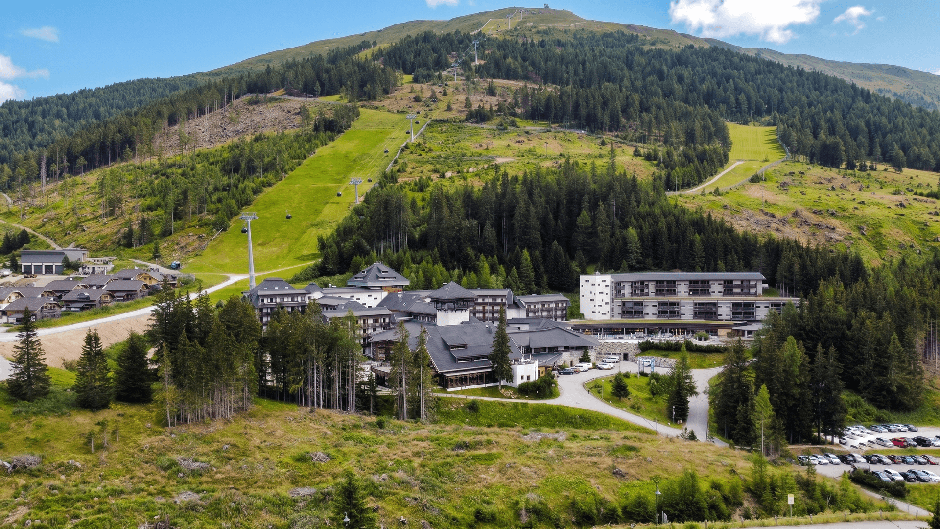 Luftaufnahme eines Hotel- oder Resortkomplexes eingebettet in eine grüne Berglandschaft.