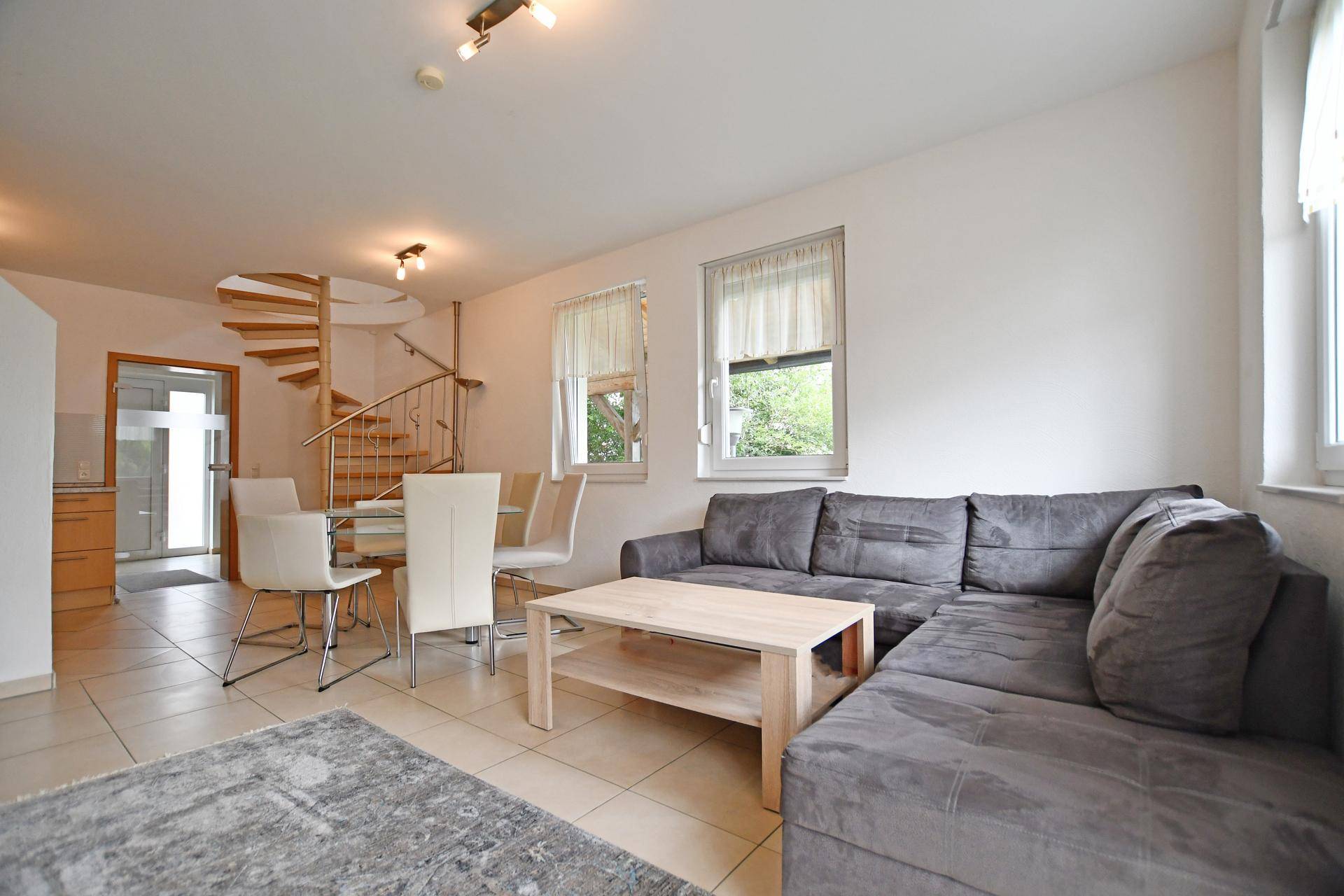 Heller Wohn- und Essbereich mit Fliesenboden und eleganter Wendeltreppe.