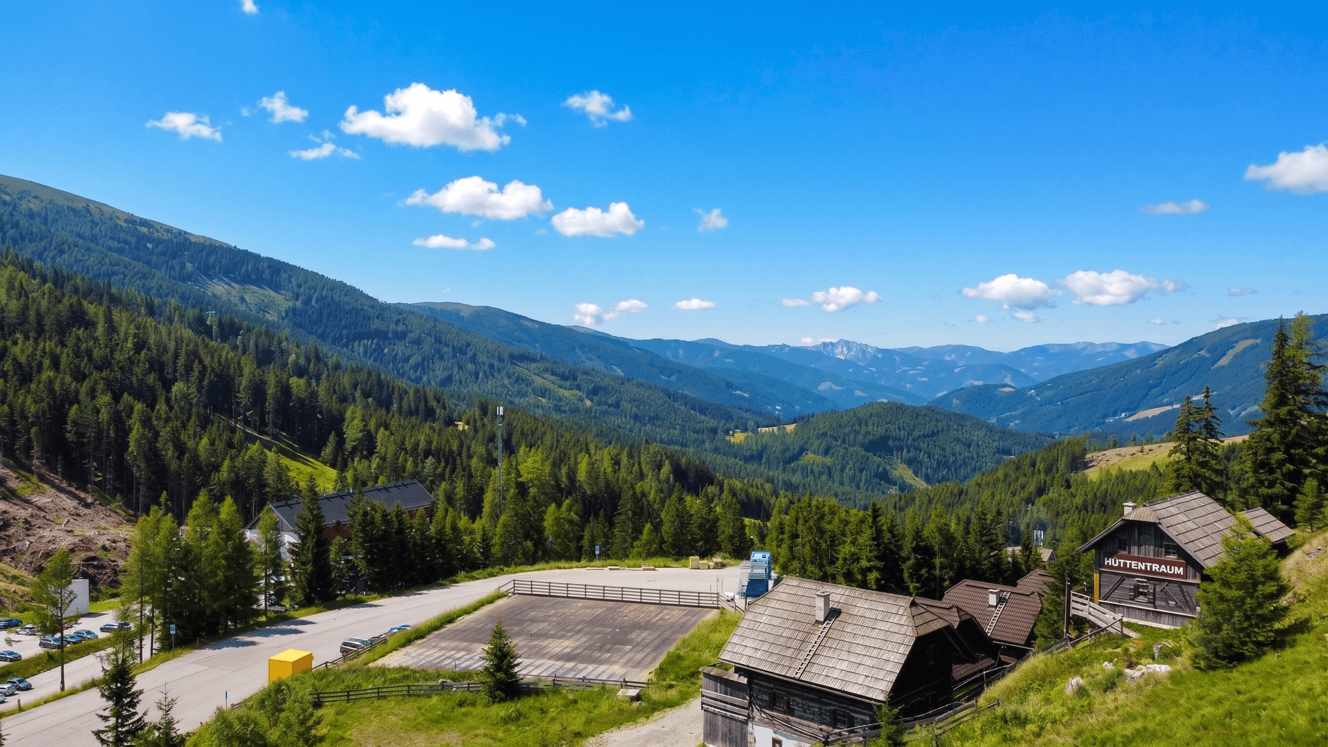 Weitläufiger Panoramablick über ein grünes Bergtal mit traditionellen Hütten unter blauem Himmel.