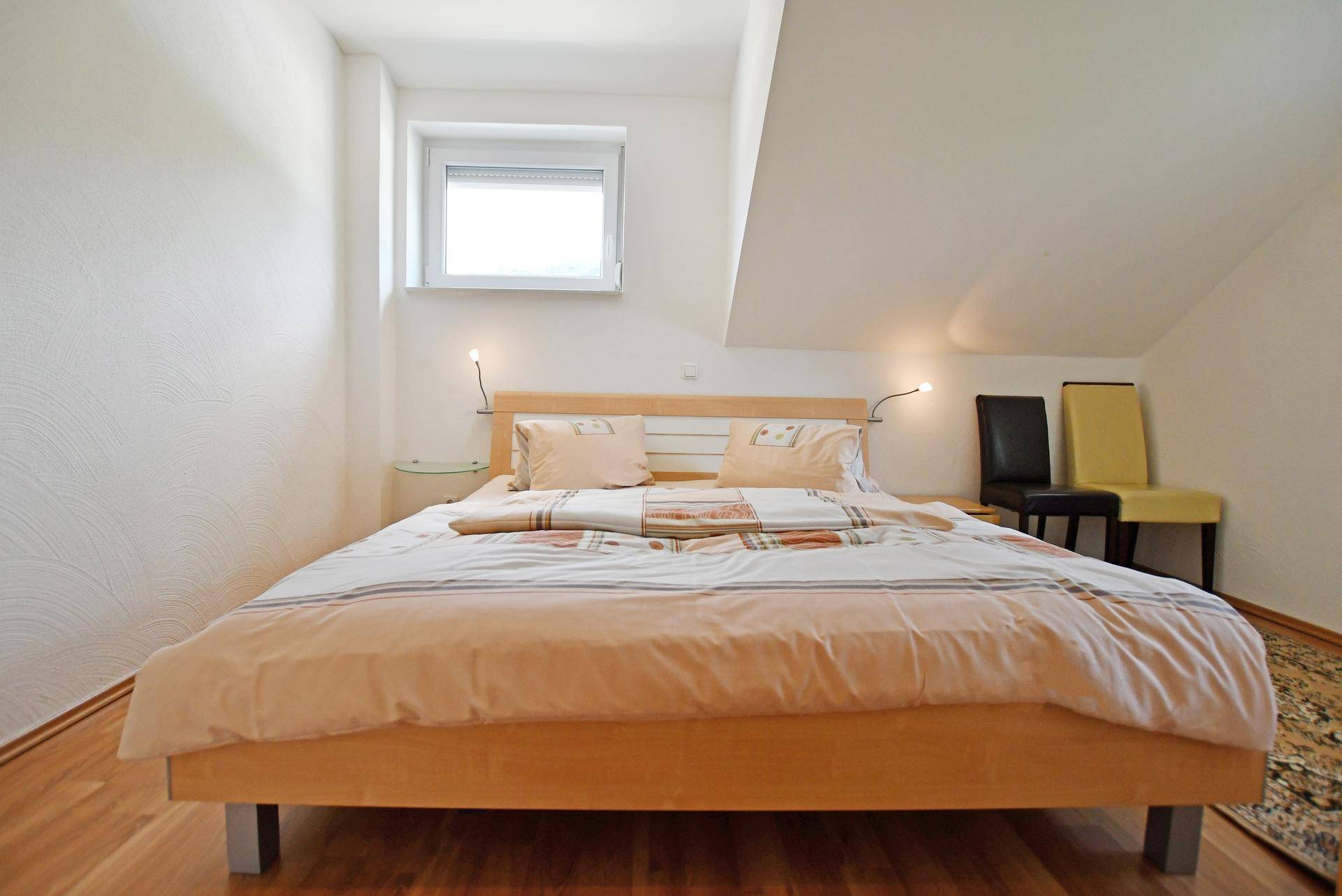 Gemütliches Schlafzimmer mit Holzboden, Dachschräge und einem Fenster.
