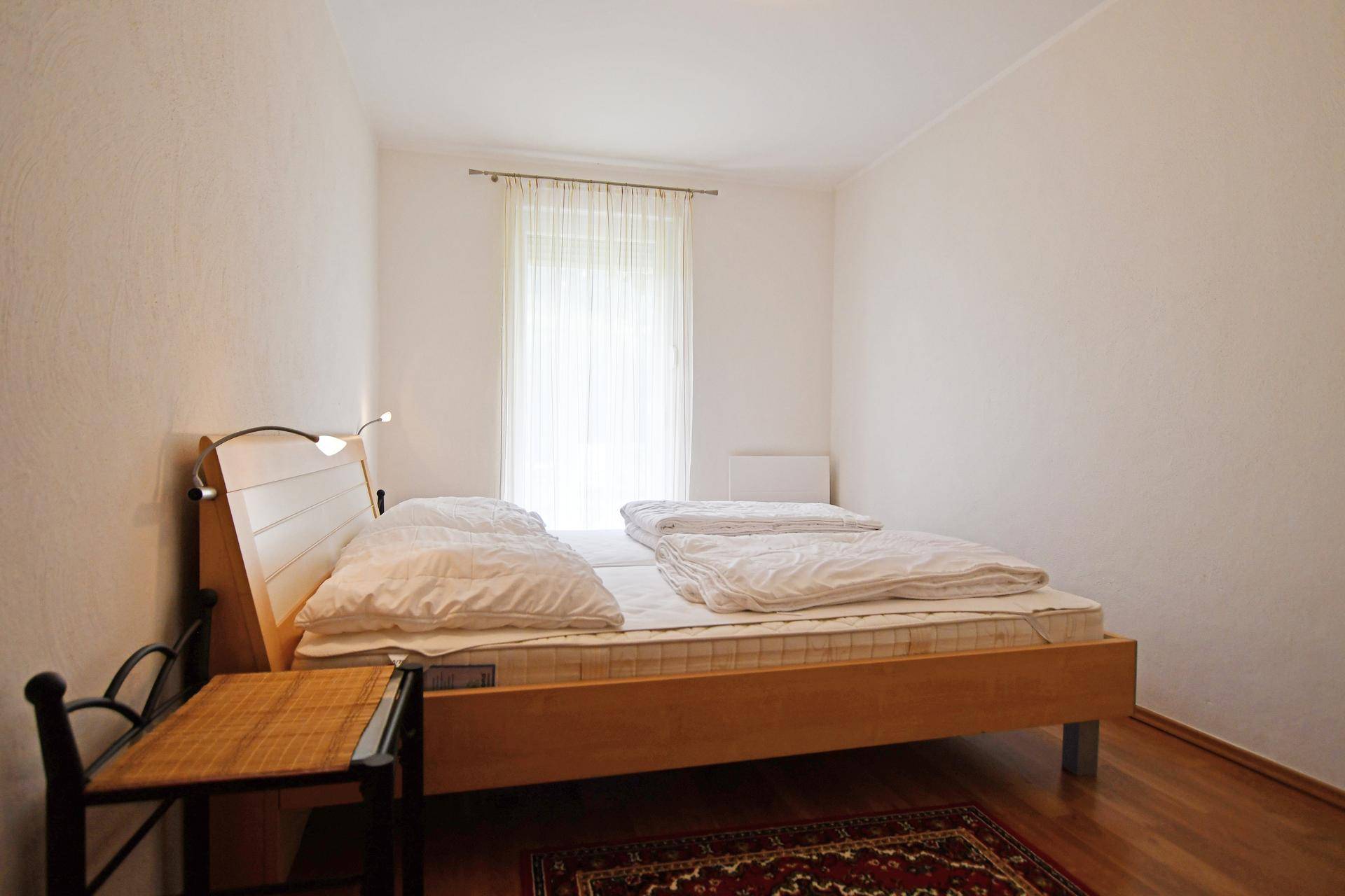 Schlichtes Schlafzimmer mit Doppelbett, Holzfußboden und hellem Fenster.