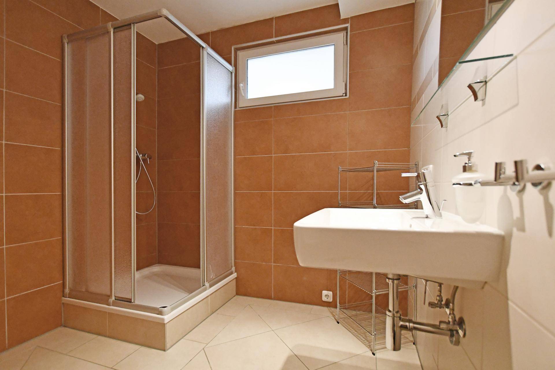 Funktionales Badezimmer mit braunen Fliesen, Duschkabine und Fenster für Tageslicht.