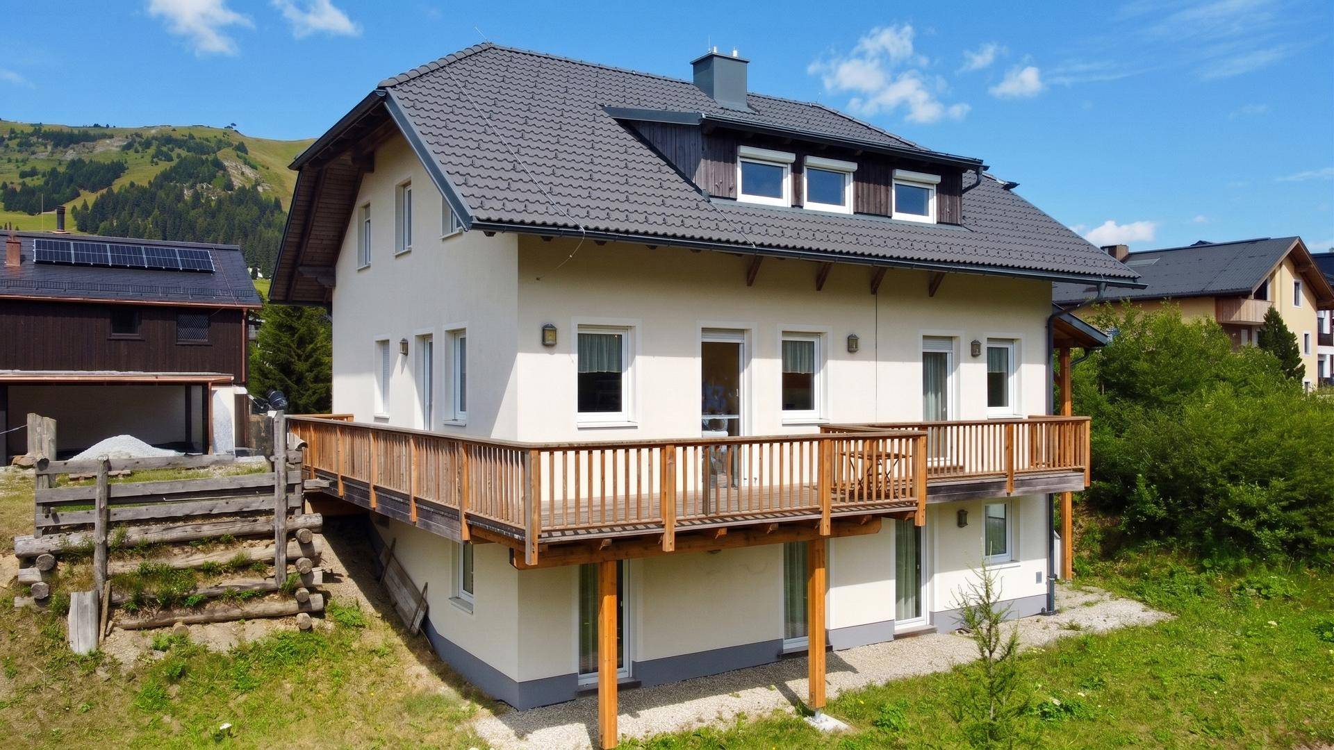 Modernes Haus mit großem Holzbalkon und Blick auf die umliegende Berglandschaft.